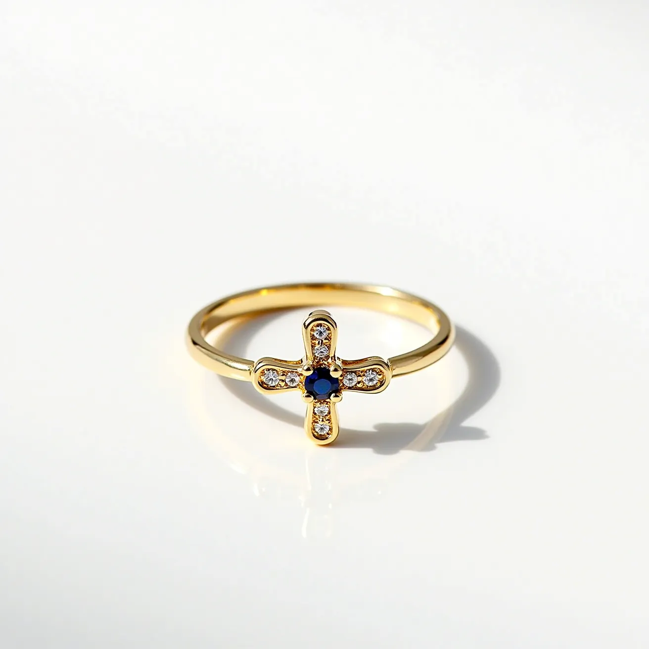 This cross ring features a gold band with a cross design at the center. The cross is adorned with small, round-cut diamonds in a pavé setting along each arm, providing a sparkling contrast to the band. At the center of the cross is a round-cut blue sapphire, set within a bezel that highlights its color. The band and cross are seamlessly joined, creating a smooth and elegant piece without any visible clasps or attachments.