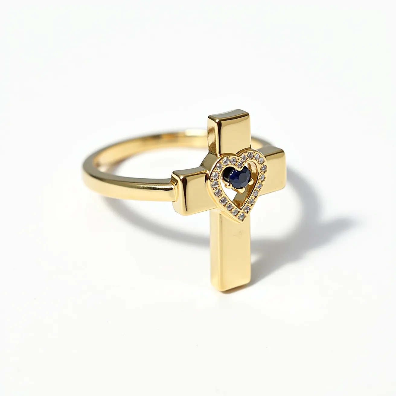 This cross ring features a sleek gold band and a prominent cross design at the front, crafted from gold material. At the center of the cross, a heart-shaped cutout is accentuated with small, round brilliant-cut diamonds set in a pavé style. Nestled within the heart is a dark blue gemstone, likely a sapphire, crafted in a heart shape as well. The overall composition is elegant yet striking, merging religious symbolism with luxurious elements.