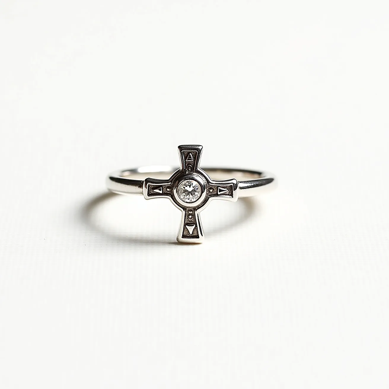 This cross ring features a sleek metal band, likely made of silver or white gold, supporting a cross-shaped centerpiece. At the heart of the cross is a round-cut gemstone, possibly a diamond, set in a bezel setting for added security and elegance. The cross design includes small triangular embellishments at each end, enhancing its visual appeal. There is no clasp or attachment, as the ring is a continuous band intended for wearing on the finger.