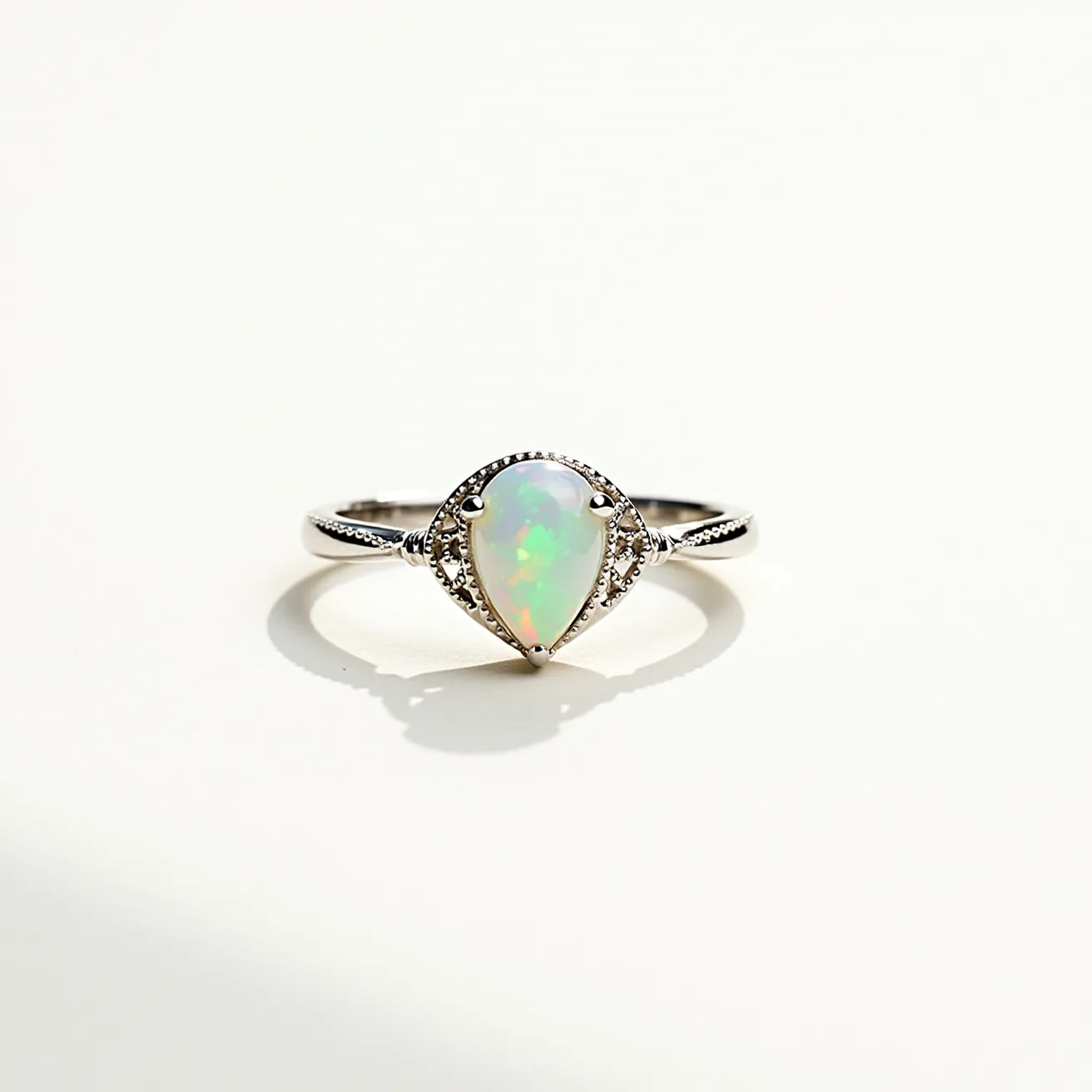 This crown ring features an elegant pear-shaped opal at its center, displaying a captivating play of colors. The opal is set in a bezel setting, which both secures and highlights the stone. The band is made of a polished metal, likely silver or white gold, complementing the opal's iridescence. Flanking the opal are small ornate metal accents on the shank, adding a decorative touch that enhances the ring's regal design. The overall appearance is both delicate and sophisticated, making it a stunning piece of jewelry.