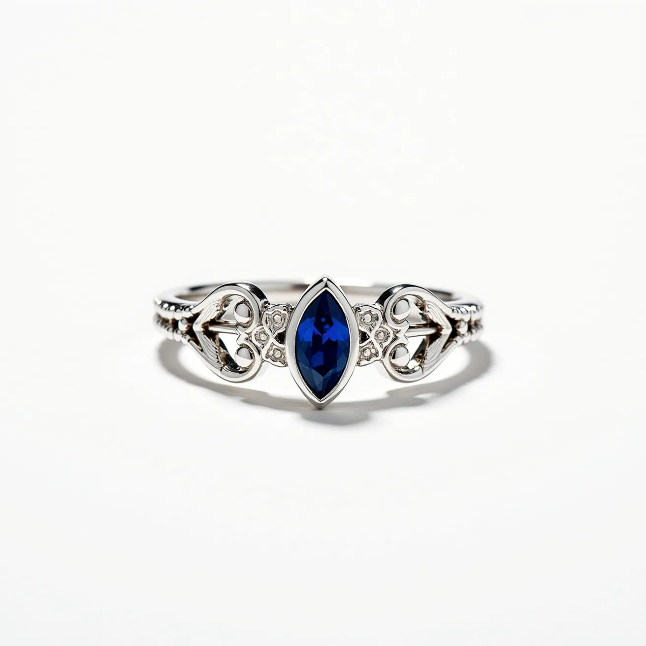 This crown ring features an elegant design crafted from a lustrous silver-toned metal, highlighted by a central marquise-cut blue gemstone that serves as the focal point. The vivid blue stone is set within a simple, polished bezel setting, enhancing its regal appearance. The band of the ring is intricately designed with delicate, flowing metalwork that resembles a crown, adding to its ornate charm. The craftsmanship showcases small milgrain details, enriching the design and giving the ring a touch of vintage appeal. The shank is smoothly finished, allowing for comfortable wear and a seamless look.