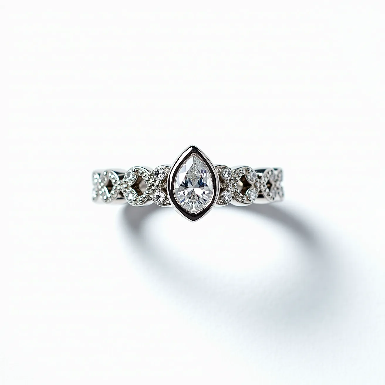 This crown ring features a beautifully crafted design with a central pear-shaped gem, likely a diamond, set in a bezel setting. The band is adorned with smaller round-cut diamonds, each held in place with a pavé setting, adding to the ring's intricate and ornate appearance. Made from a lustrous metal, possibly white gold or platinum, the ring exhibits a luxurious and elegant finish. The integration of these elements creates a regal and sophisticated aesthetic, befitting a crown-inspired design that exudes elegance and charm.