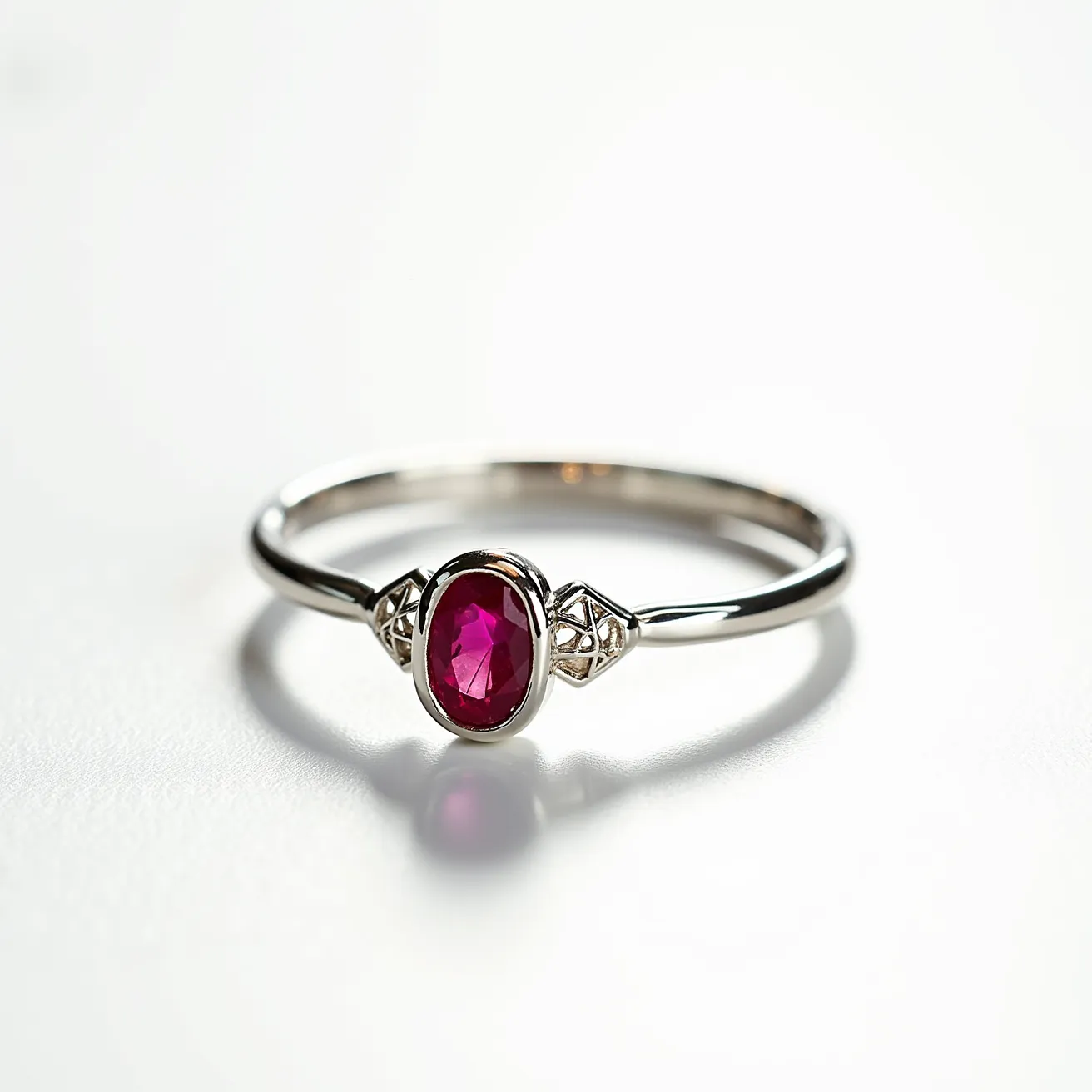 This custom ring features a sleek, shiny metallic band, likely crafted from a precious metal such as white gold or platinum. It is adorned with an oval-cut red gemstone, appearing to be a ruby, which is centrally positioned in a bezel setting. On either side of the ruby, there are geometric embellishments that add an elegant touch to the design. The simplicity of the band highlights the beauty of the central stone, making it a striking piece of jewelry that exhibits both classic and modern design elements.