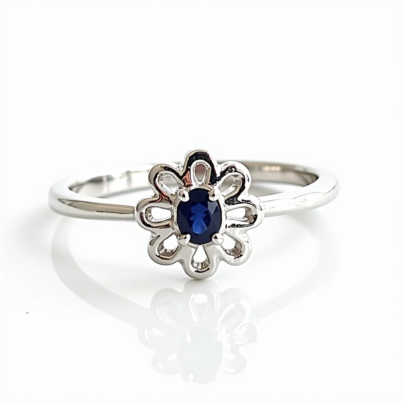 This daisy ring features a flower-like design crafted from a polished silver metal. At the center of the daisy, an oval-cut blue gemstone is set, likely a sapphire, adding a vibrant contrast to the silver petals that surround it. The gemstone is securely held in place with a bezel or a simple prong setting that complements the delicate design of the petals. The band of the ring is slender and smooth, enhancing the elegance of the overall piece. This design merges simplicity with a touch of sophistication, making it a versatile accessory.