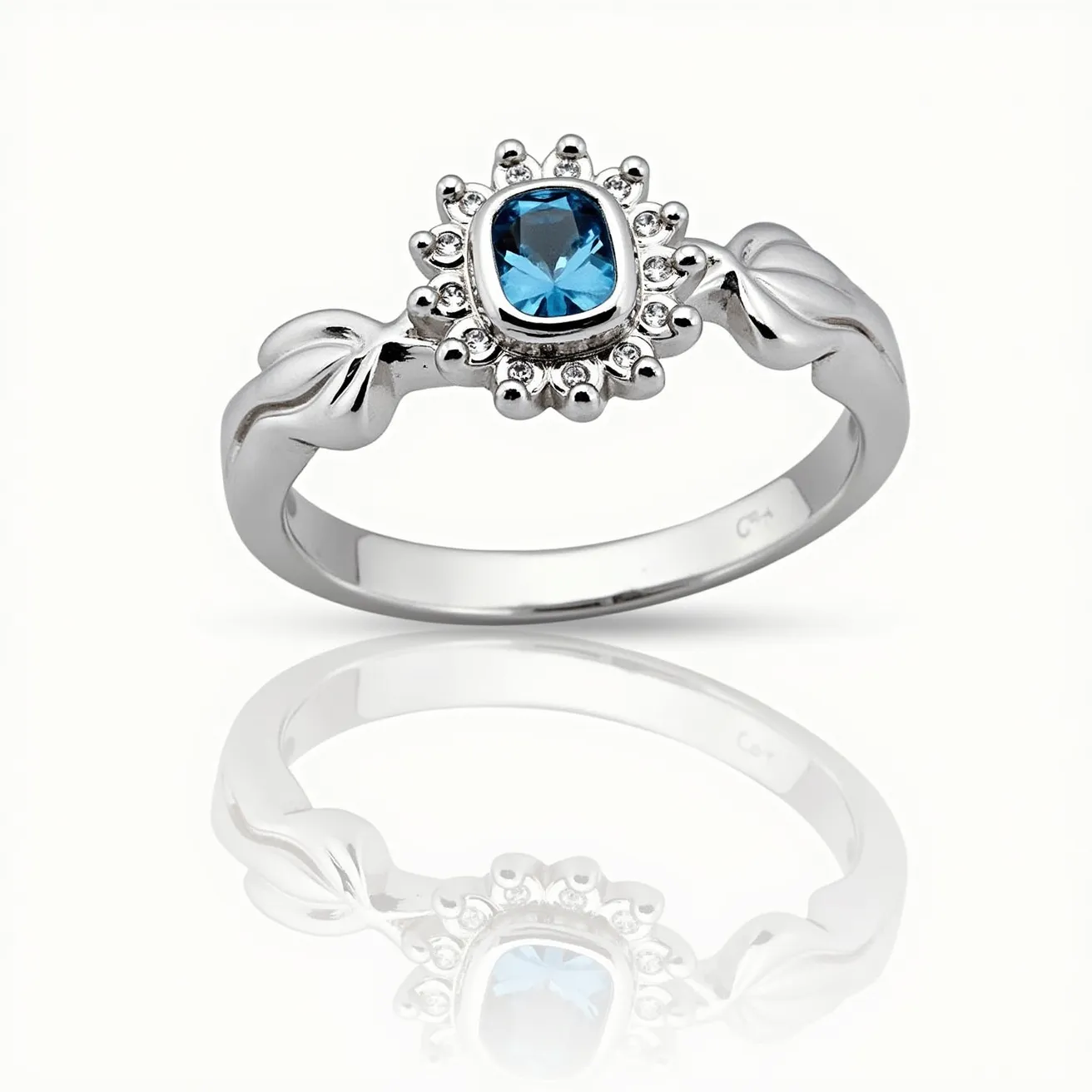 This daisy ring features a silver band with a distinctive floral design. At the center, there is a cushion-cut blue gemstone, bezel-set, which serves as the focal point. Surrounding the central gem are small bead-like details that mimic petals, enhancing the daisy motif. The band showcases elegant, leaf-like accents on either side of the setting, adding to the organic, nature-inspired aesthetic of the piece. The ring lacks any additional clasps or attachments, designed for a seamless and elegant appearance on the finger.