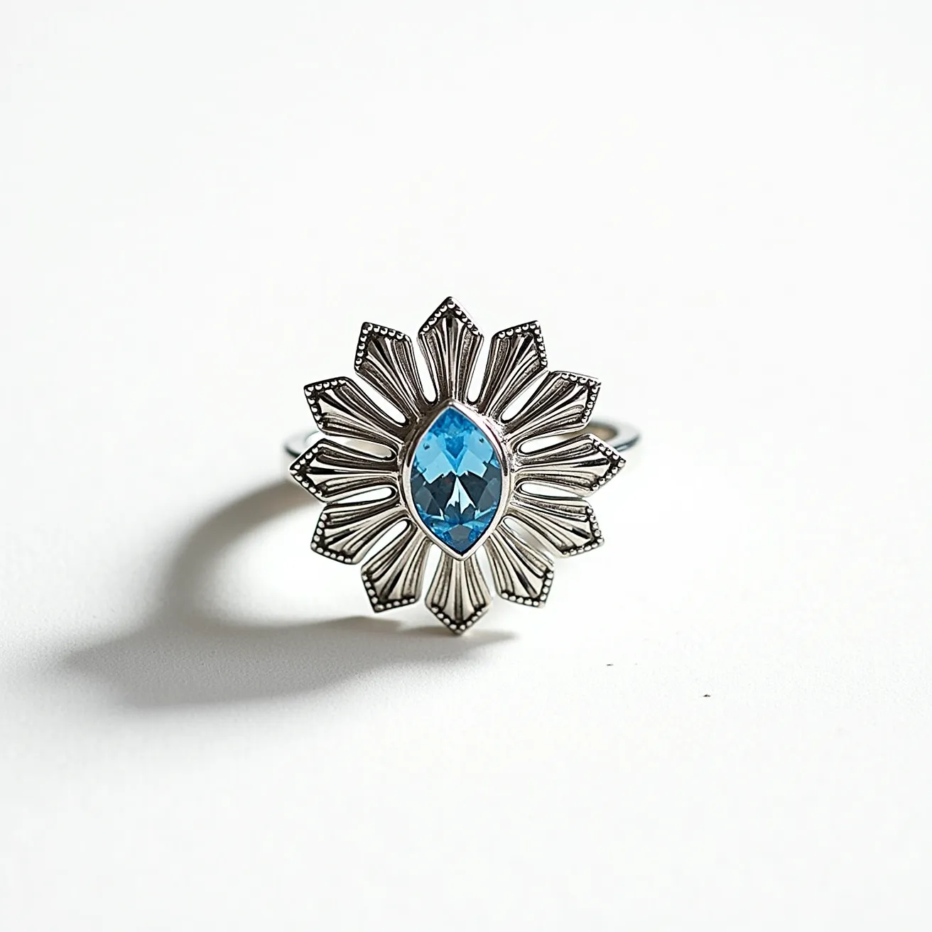 This daisy ring features a striking design with a central marquise-cut blue gemstone, likely a topaz, set in a secure bezel. The intricate petals are crafted from a lustrous metal, possibly silver, radiating from the center stone with a detailed, textured pattern. The band of the ring is smooth and unadorned, complementing the ornate floral motif.