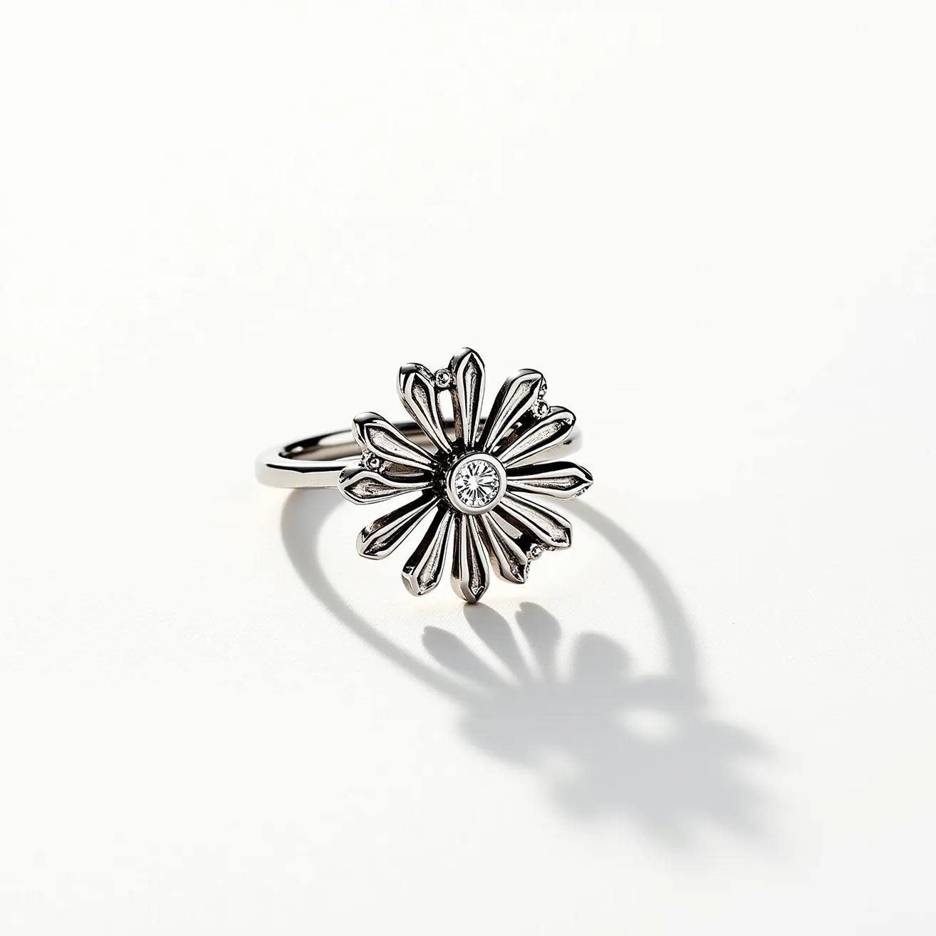 This daisy ring features a central gemstone, likely a round-cut diamond, set in a bezel setting, adding a touch of brilliance to the floral design. The petals of the daisy are crafted from what appears to be a metal, possibly silver or white gold, and are elegantly detailed to enhance the overall aesthetic of the ring. The band complements the floral motif by remaining simple and sleek, allowing the daisy to be the focal point. The craftsmanship of the ring highlights a harmonious blend of nature-inspired artistry and quality materials.