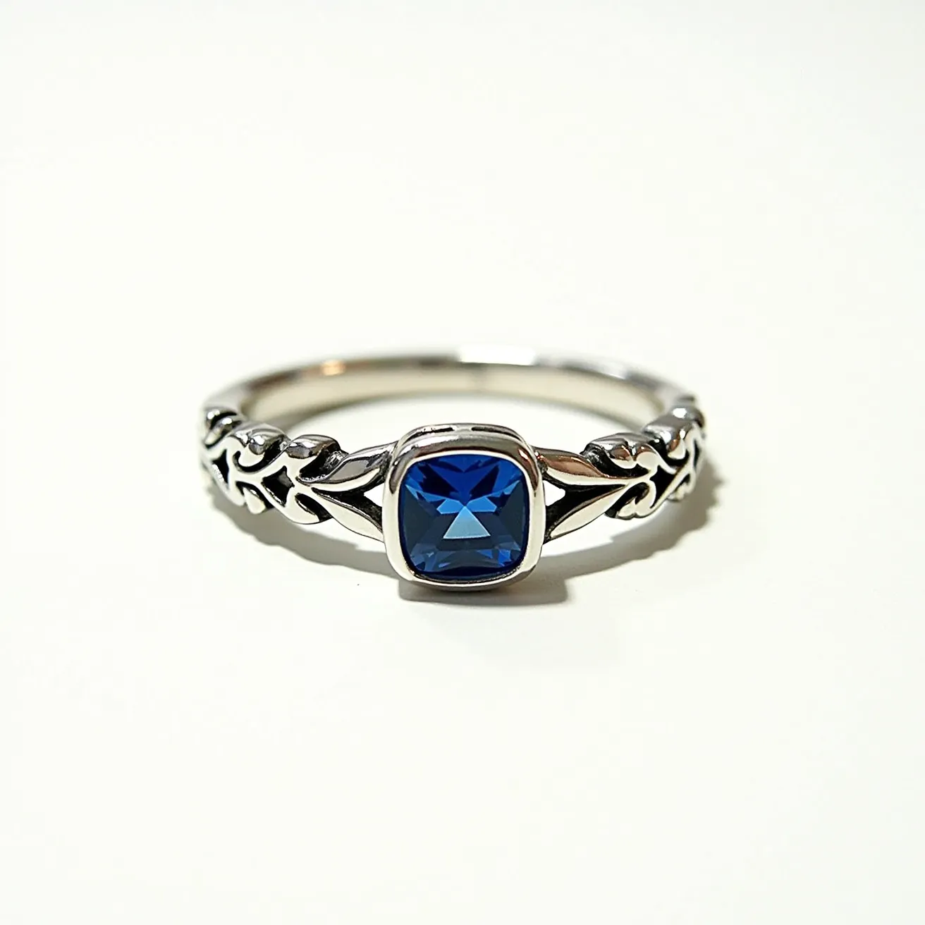 This December birthstone ring features a captivating blue gemstone, likely a zircon or turquoise, which are traditional for this month. The stone is cut in a cushion shape and is elegantly set in a bezel setting, enhancing its secure placement and modern aesthetic. The band is crafted from what appears to be a polished metal, possibly sterling silver, adorned with intricate vine-like engravings that add an organic and delicate touch to its design. The ring showcases a harmonious blend of boldness and elegance, ideal for those born in December or anyone with an affinity for the deep, alluring hue of its central gemstone.