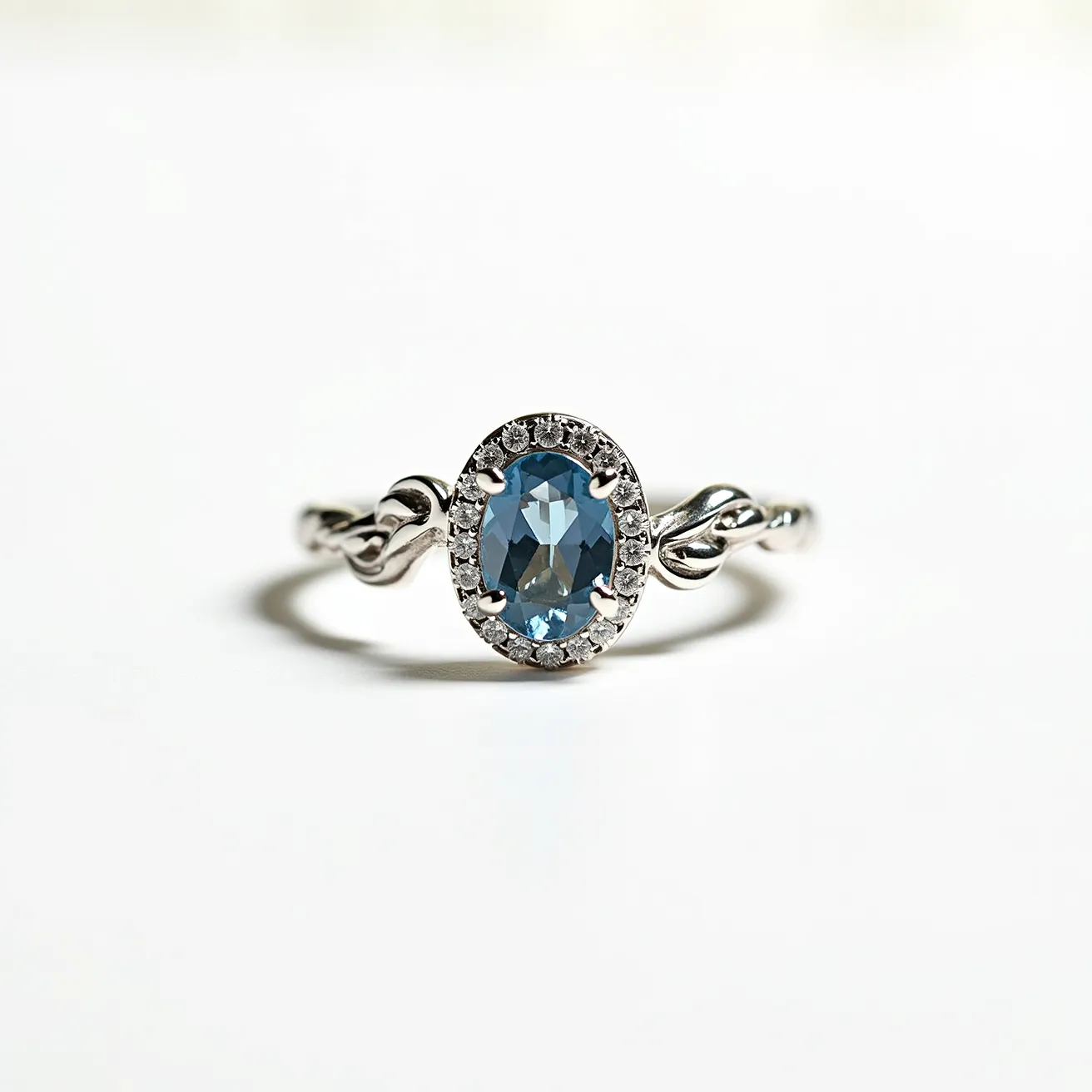 This December birthstone ring features a captivating oval-cut blue topaz at its center, embodying the traditional birthstone for the month. The topaz is elegantly encircled by a halo of small, sparkling clear stones, likely diamonds or cubic zirconia, set in a shimmering metal band that could be silver or white gold. The band itself showcases a twisted design, adding a touch of elegance and sophistication to the piece. The prong setting securely holds the central gemstone, ensuring durability and showcasing the stone’s brilliance. The overall design harmoniously combines simplicity with delicate detailing, highlighting the beauty of the birthstone.