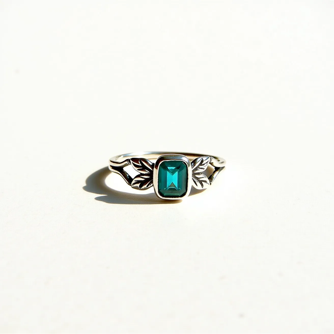 This December birthstone ring features a striking blue topaz gemstone, which is December's traditional birthstone, cut into a rectangular shape with a faceted surface that enhances its brilliance. The gem is elegantly bezel-set within a refined silver band, providing a modern and secure setting. Flanking the gemstone are intricate metalwork details resembling leaves or feather motifs, adding an artistic and nature-inspired touch to the design. The sleek band and setting are polished to a high shine, emphasizing the ring's elegant and sophisticated aesthetic.