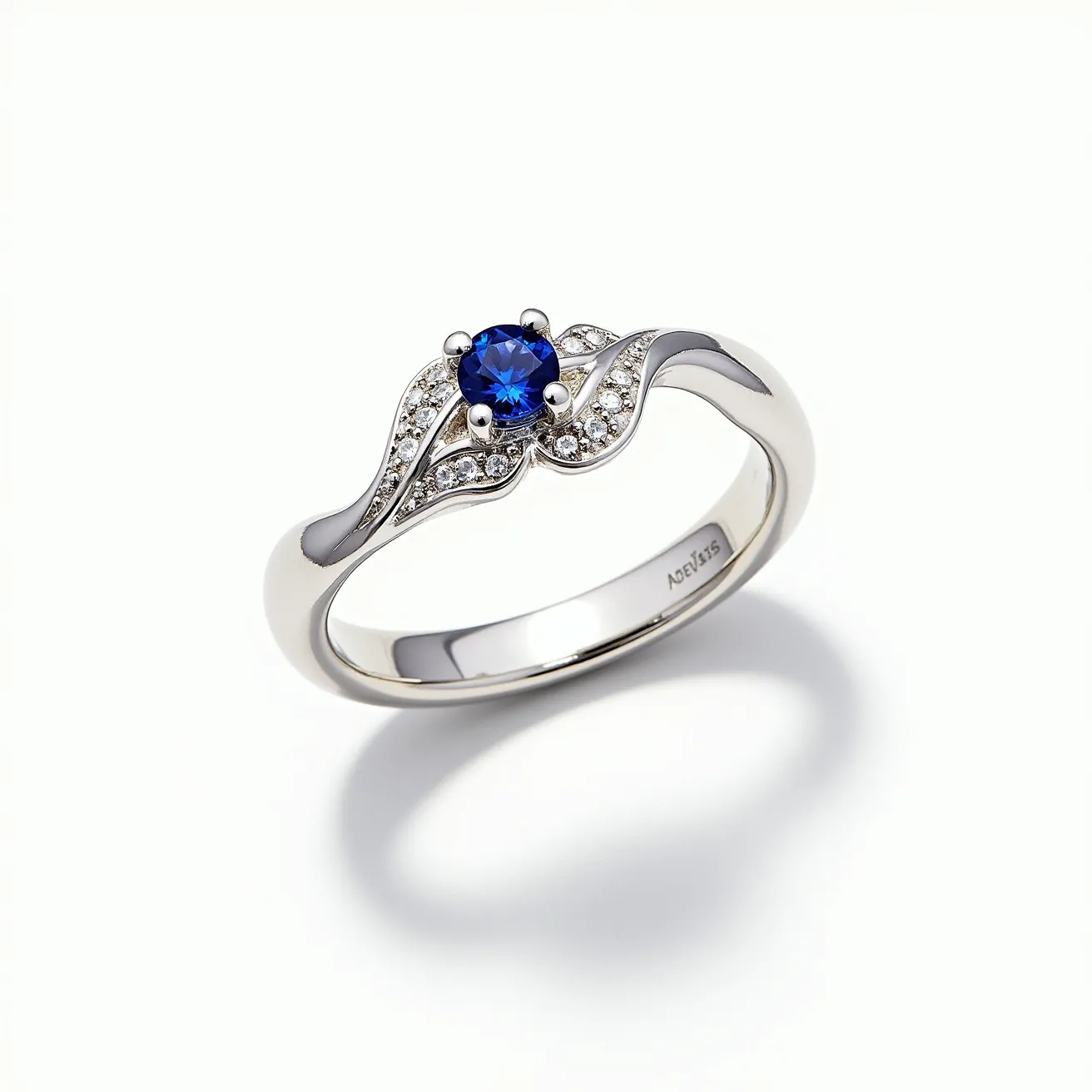 This December birthstone ring features a stunning round-cut blue stone, likely representing a blue topaz or zircon, set at its center. The stone is held securely by a four-prong setting, enhancing its brilliance. Surrounding the central gemstone are small, sparkling clear stones, possibly diamonds or cubic zirconia, intricately set into a delicate, wave-like design that adds elegance and sophistication to the piece. The band appears to be made of sterling silver, as indicated by the visible "925" engraving, providing a sleek and shiny finish that complements the vibrant blue center stone.