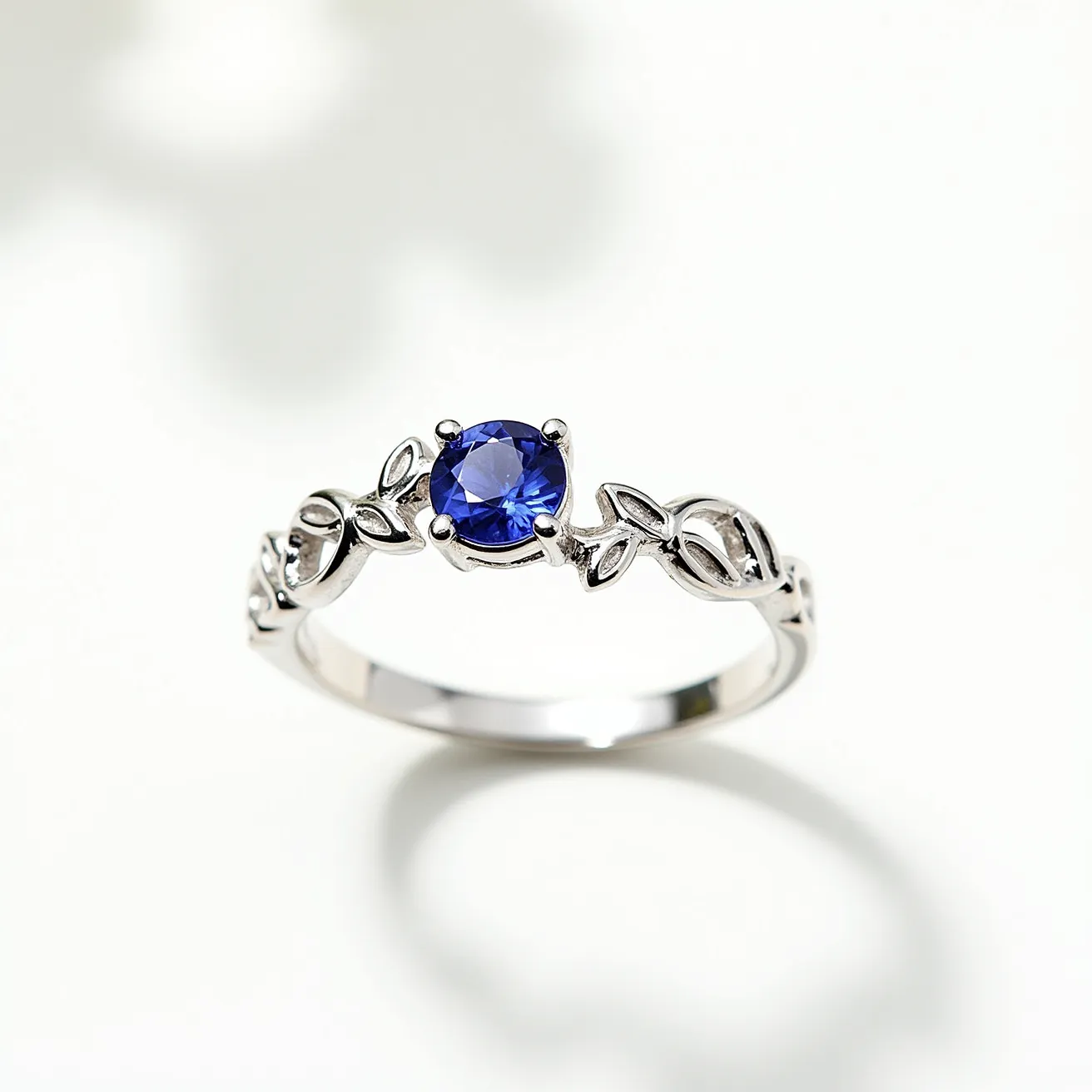 This December birthstone ring features a beautifully cut round blue gemstone, which is likely a tanzanite or turquoise, both of which are traditional birthstones for December. The stone is securely set in a classic four-prong setting that allows maximum visibility and light to highlight its vibrant hue. The band is crafted from a polished metal, possibly silver or white gold, and showcases an elegant design with leaf-like motifs that enhance the stone's natural beauty. Overall, the ring presents a harmonious blend of gemstone allure and refined metalwork.