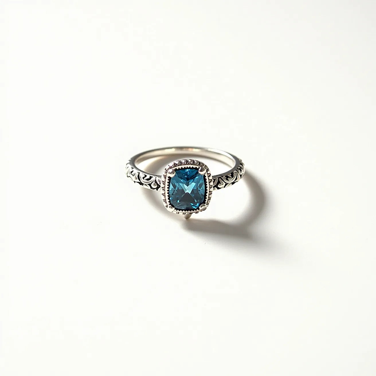 This December birthstone ring features a striking blue topaz gemstone, expertly cut into a cushion shape, held securely by a bezel setting. The band is crafted from sterling silver, exhibiting intricate and ornate detailing that adds a touch of elegance to the overall design. The gemstone's rich, blue hue is complemented beautifully by the silver band, making it both a captivating and stylish piece of jewelry.