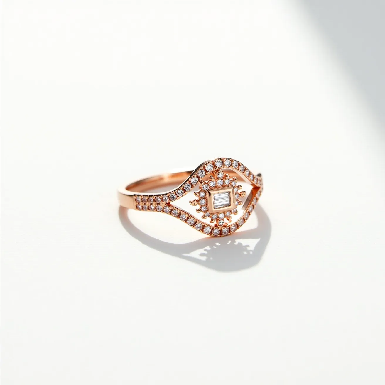 This diamond ring features a captivating design with a rose gold band. The centerpiece is a rectangular, baguette-cut diamond set within an intricate eye-shaped design. Surrounding the central stone is a halo of small round diamonds, adding brilliance and elegance to the setting. The eye motif extends with additional pavé-set diamonds along the top and bottom curves, emphasizing both style and sophistication. The ring is artistically crafted without the need for a clasp or extra attachment, showcasing its sleek and cohesive aesthetic.