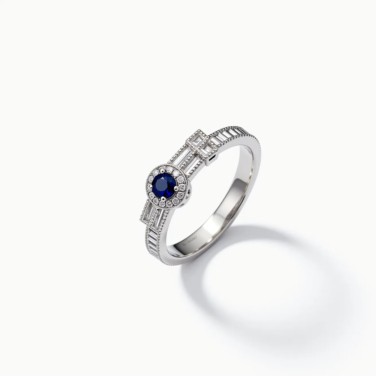 This diamond ring features a striking design highlighted by a central round-cut blue sapphire set in a bezel surrounded by small round diamonds, creating a halo effect that enhances its brilliance. The band is crafted from what appears to be white gold or platinum, adorned with baguette-cut diamonds set along the shank in a channel setting, adding to the ring's sophisticated allure. The precise cuts and settings highlight the pristine quality of the gemstones, while the metallic band provides a lustrous and refined finish. The overall aesthetic offers a blend of classic elegance and modern sophistication.