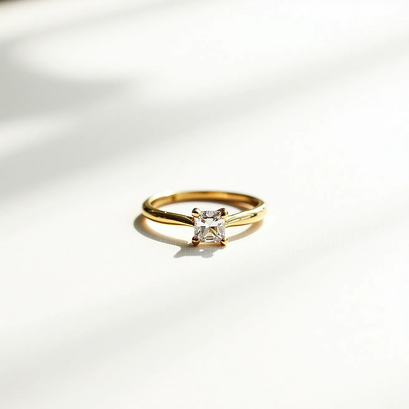 This diamond wedding band showcases a sleek gold band, elegantly supporting a solitaire diamond at its center. The gemstone is a square cut, suggesting the possibility of an Asscher or princess cut, set in a classic four-prong setting that offers both security and an open view of the diamond's brilliance. The simplicity of the band enhances the diamond's prominence, creating a timeless and sophisticated look.