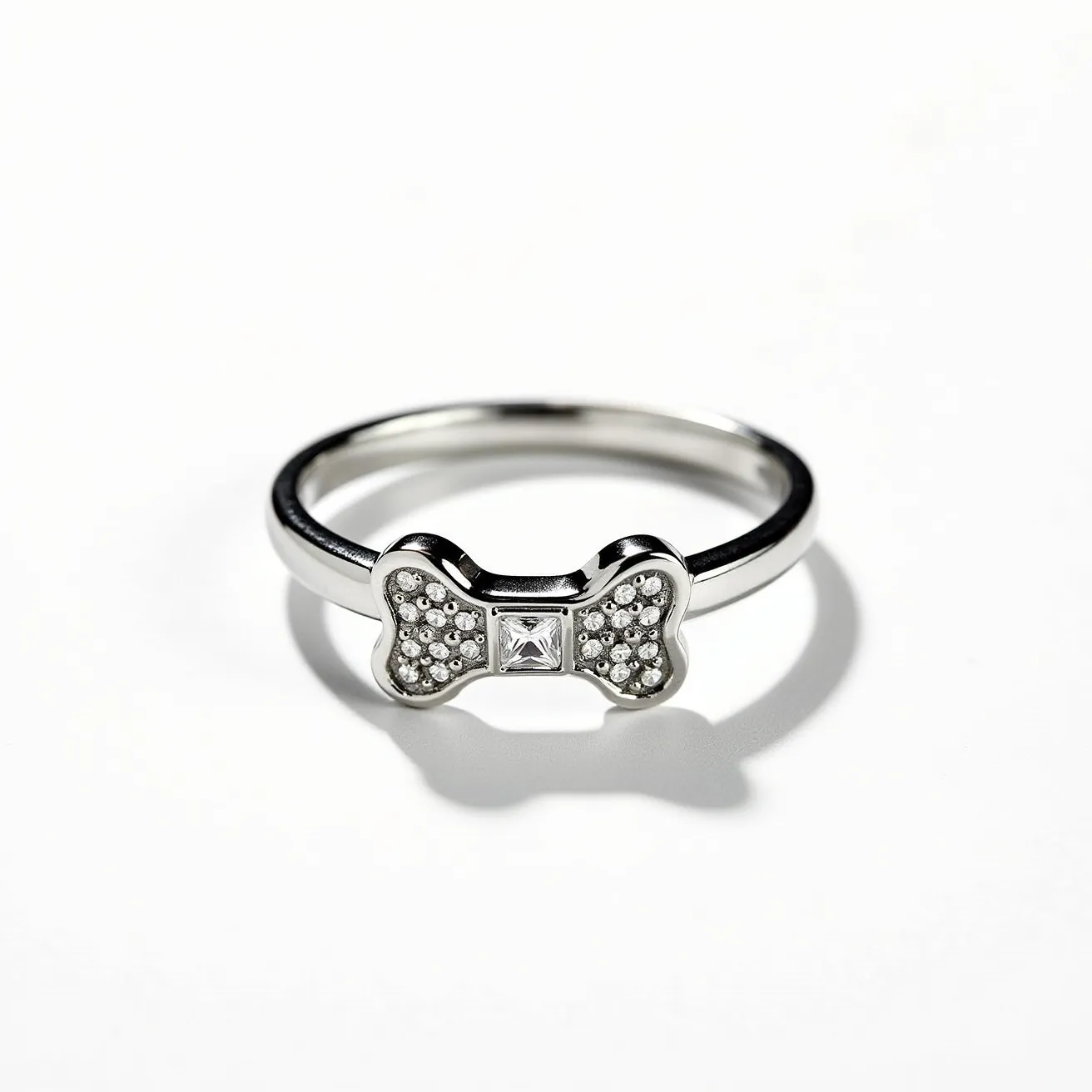 This dog ring features a stylish design crafted from a polished metal, likely sterling silver or white gold. At the center is a bone-shaped motif adorned with small, round, pave-set stones that resemble diamonds, adding a touch of sparkle. In the middle of the bone is a square-cut gem, also likely a diamond, set prominently to catch the light. The ring does not seem to have any specific clasp or attachment as it is designed to be worn as a typical finger ring.