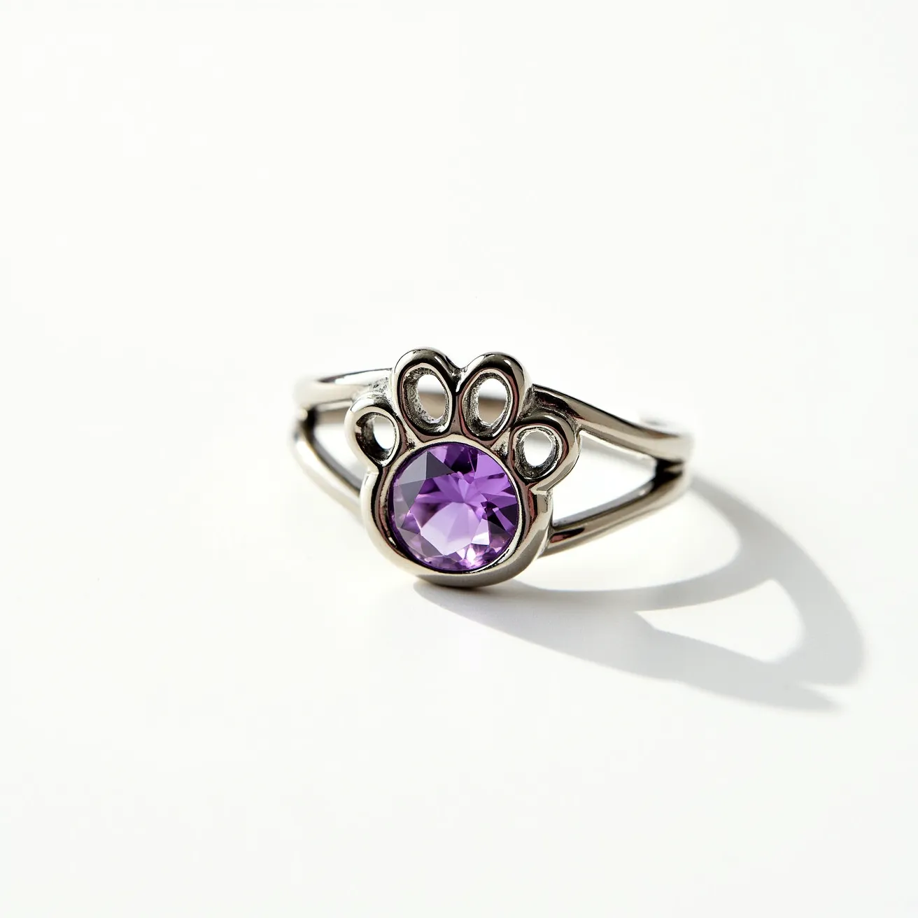 This dog ring features a polished metal band, likely silver or white gold, that forms an elegant paw print design. At the center of the paw print is a round, faceted purple gemstone set in a secure bezel setting, showcasing the gem's vibrant color and clarity. There is no visible clasp or additional attachment, suggesting a continuous band structure. The combination of the lustrous metal and the striking gemstone creates a charming and eye-catching piece of jewelry.