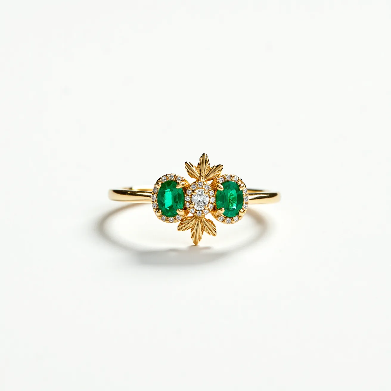 This emerald birthstone ring features a delicate band crafted from gold, showcasing a trio of gemstones. At its center lies a round-cut diamond, securely set in a prong setting, flanked by two oval-cut emeralds. The emeralds are similarly encased in prong settings, their rich green hues highlighting the central diamond. The arrangement is complemented by leaf-like gold details extending outward, adding an elegant touch to the overall design.