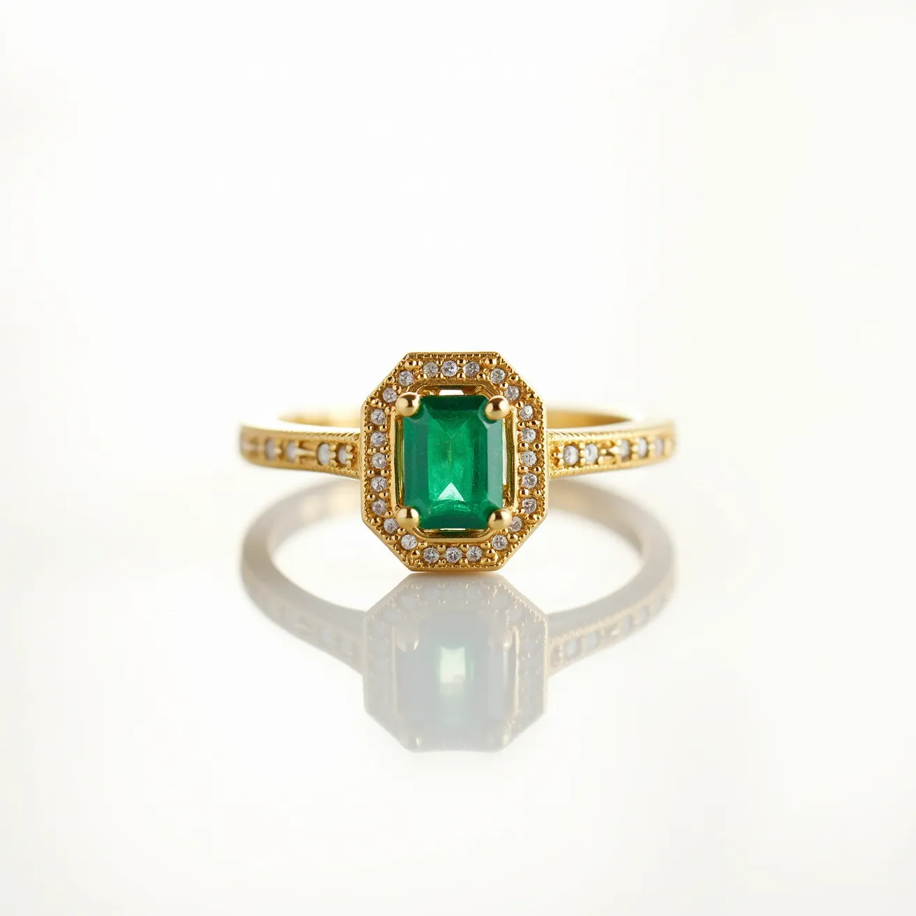 This emerald engagement ring features a central emerald-cut green gemstone set in a yellow gold band. The emerald is framed by a halo of small, sparkling round diamonds, enhancing its vibrant color and rectangular shape. The band itself is adorned with additional diamonds, set into the metal to add extra brilliance and elegance. The setting employs a four-prong design to securely hold the central emerald in place, ensuring both stability and prominence.