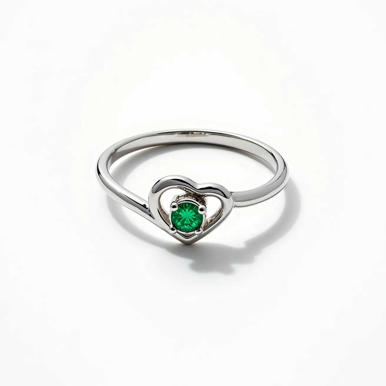 This emerald promise ring features a delicate band crafted from what appears to be a polished silver or white gold material. The focal point of the design is a vibrant, round-cut emerald gemstone, which is securely set within a heart-shaped setting. The emerald is held in place by four prongs, ensuring stability and creating a classic yet elegant appearance. The simplicity of the setting allows the gemstone’s deep green hue to stand out beautifully against the metallic band. The ring does not include any additional detailing, keeping the design clean and focused on the central gem.