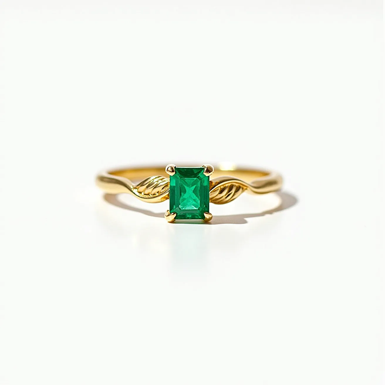 This emerald promise ring features a rectangular-cut emerald as its centerpiece, set gracefully in a four-prong setting. The band is made of polished gold, designed with delicate leaf accents on either side of the emerald, adding an element of natural elegance. The simplicity of the design highlights the vivid green hue of the emerald, making it the focal point. The artistic twists in the band lend a unique charm, ensuring a secure fit and an enchanting appearance.