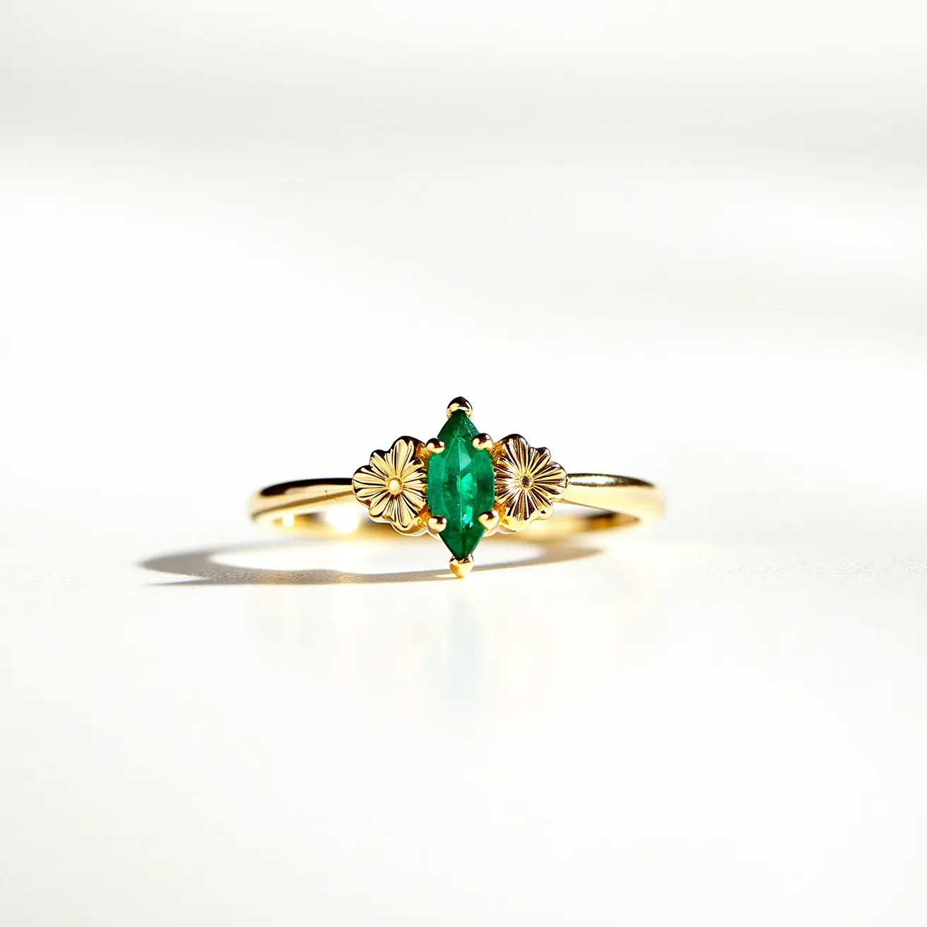 This emerald promise ring features a central marquise-cut emerald, prominently set in a secure four-prong setting. Flanking the emerald on either side are two intricately detailed gold flowers, adding an elegant and decorative touch to the design. The band of the ring is crafted from polished gold, providing a classic and refined finish to the piece. The overall design showcases a harmonious blend of vibrant color and delicate artistry, making it a beautiful symbolic piece.