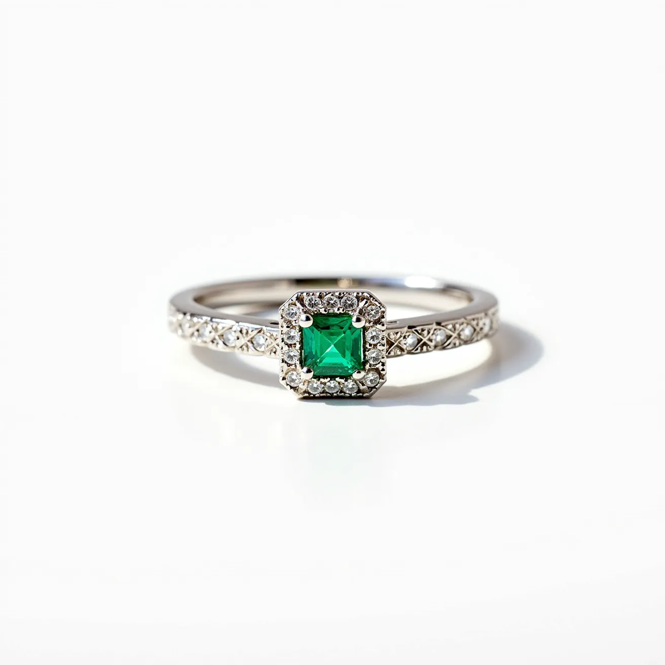 This emerald ring features a vibrant, square-cut emerald as the centerpiece, set in a halo of small, sparkling diamonds. The emerald is notably brilliant, showcasing its rich green hue. The surrounding diamonds are delicately set, enhancing the overall radiance and providing contrast to the central stone. The band appears to be made of polished white gold or platinum, featuring an intricate design with additional small diamonds inset along its length. The craftsmanship is meticulous, with a secure prong setting for the central emerald and a sleek, elegant band design, adding a classic yet sophisticated touch to the piece.