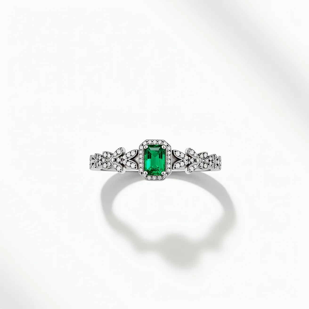 This emerald ring features a striking, rectangular emerald-cut green gemstone set in the center, showcasing its vibrant hue. The emerald is encircled by a delicate halo of small, round diamonds, adding a touch of sparkling elegance. The band is crafted from a lustrous metal, likely white gold or platinum, and is intricately adorned with additional small diamonds that form a leaf-like pattern leading up to the central setting. The detailed craftsmanship of the band enhances the overall luxurious appearance of the piece, seamlessly integrating the radiant emerald with its surrounding embellishments.