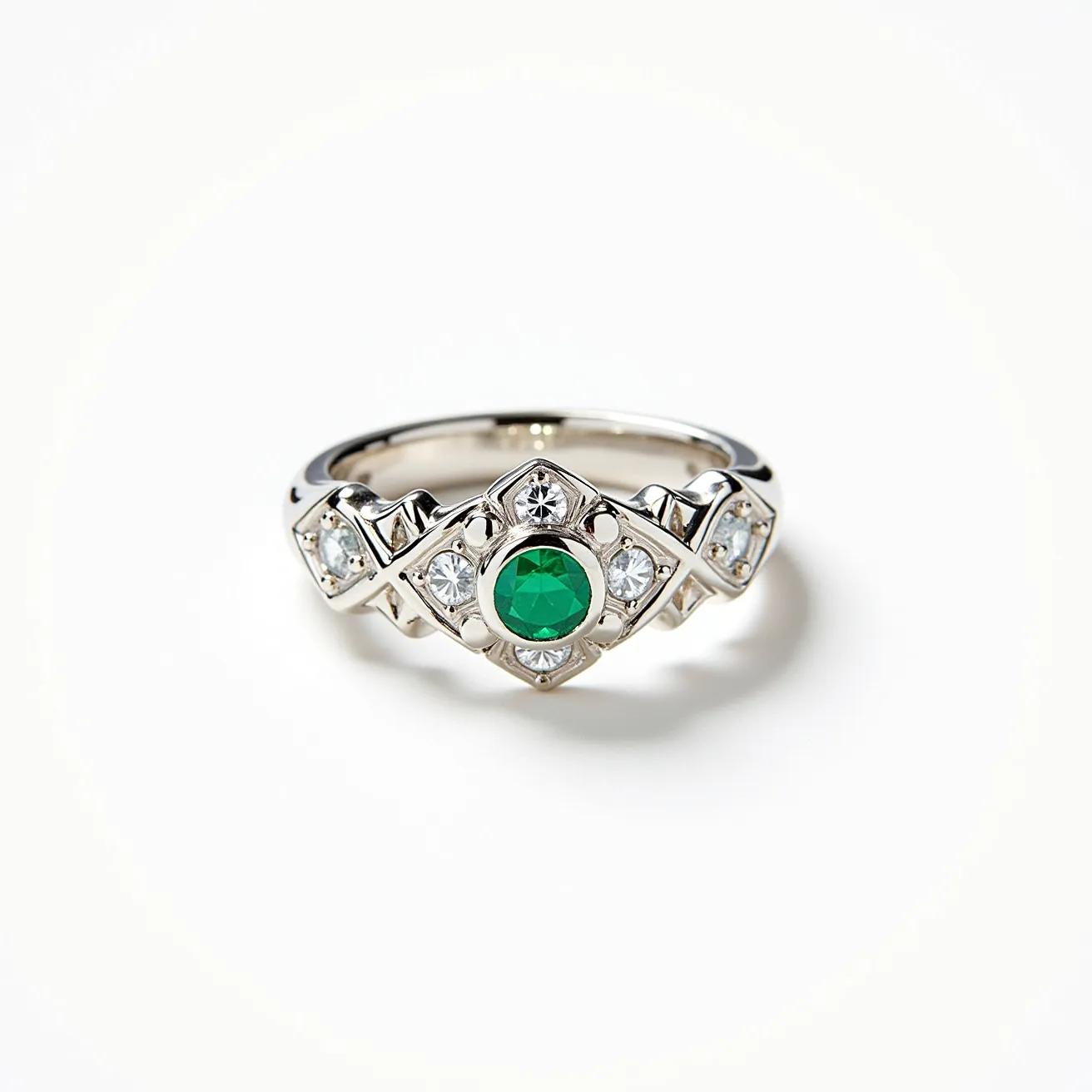 This emerald ring showcases a striking central green emerald, cut in a round shape and set securely within a bezel setting, which enhances its vibrant color. Surrounding the emerald are smaller clear stones, likely diamonds, also round-cut and arranged in a decorative pattern on the ring's band. The band itself appears to be made from a polished white metal, such as white gold or platinum, which complements the sparkle of the stones. The overall design of the ring combines elegance with a touch of intricate detailing, making it a captivating piece of jewelry.