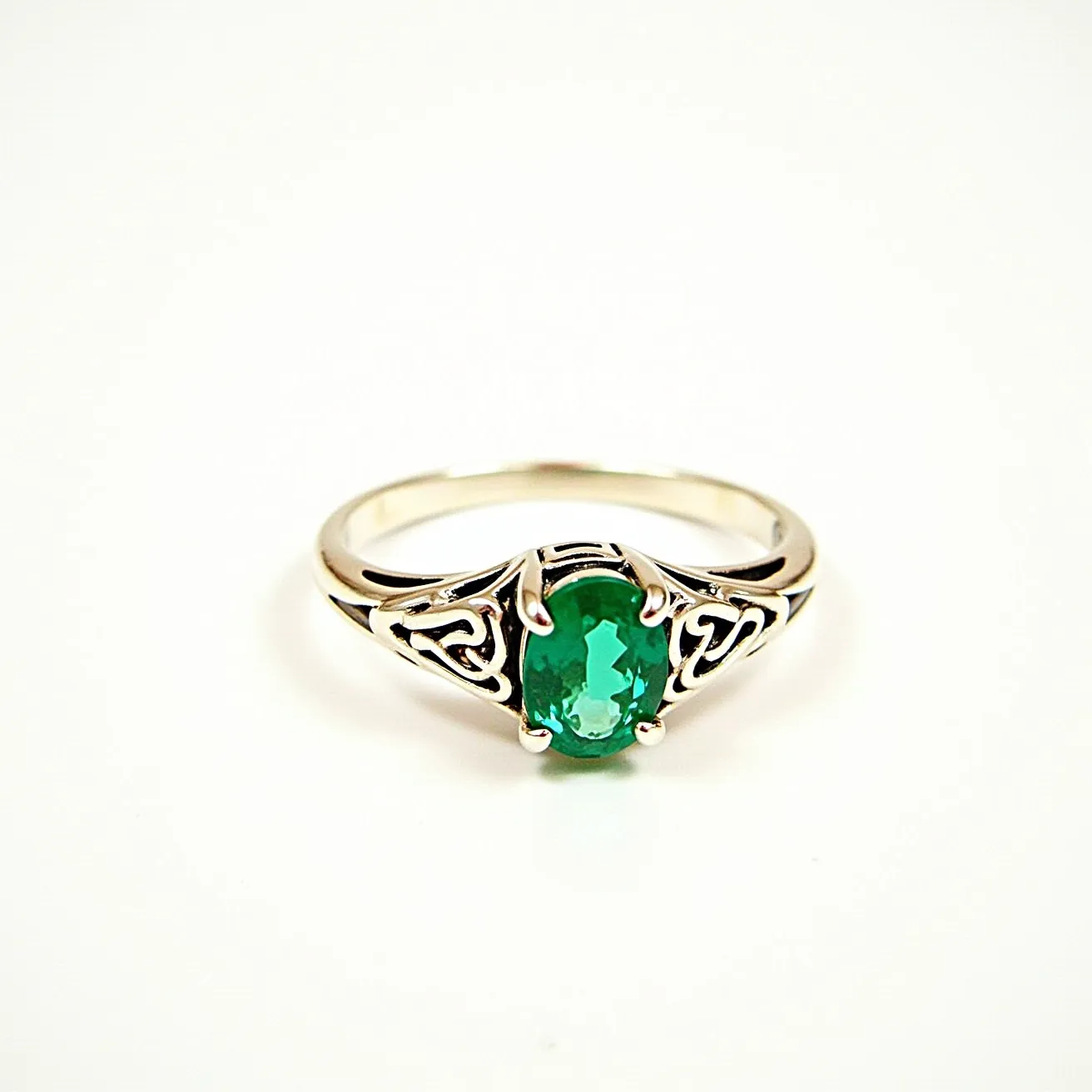 This emerald ring features a vibrant, oval-cut green emerald as its centerpiece, expertly set in a prong setting that allows maximum light to enhance the stone's natural brilliance. The band exhibits intricate silver metalwork with decorative patterns on either side of the emerald, adding an artistic and elegant touch to the overall design. The smooth, polished shank complements the intricacy of the setting, highlighting the central gemstone while providing comfort and style for the wearer.