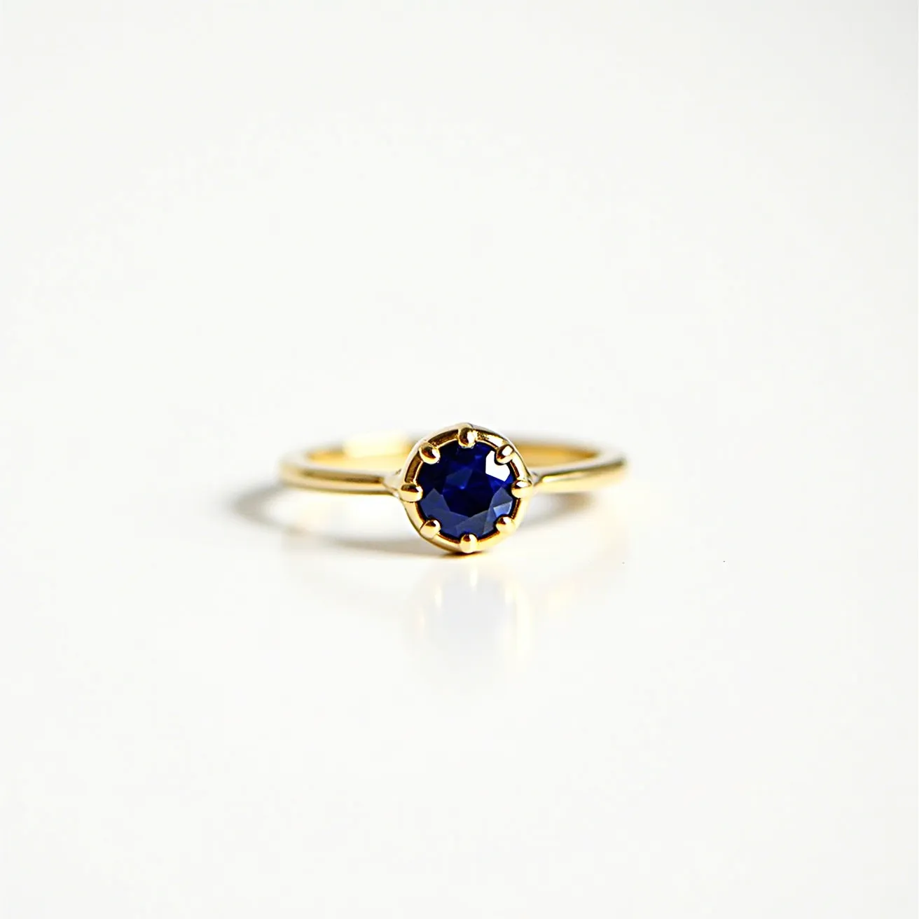 This engagement ring features a slender gold band highlighting a deep blue gemstone, most likely a sapphire. The stone is cut in a round shape and is elegantly set in a prong setting, which secures the gem while maximizing its exposure to light. The prong setting enhances the ring’s classic and sophisticated appeal, making it both timeless and stunning. The choice of a gold band adds a luxurious touch, complementing the rich hue of the sapphire.