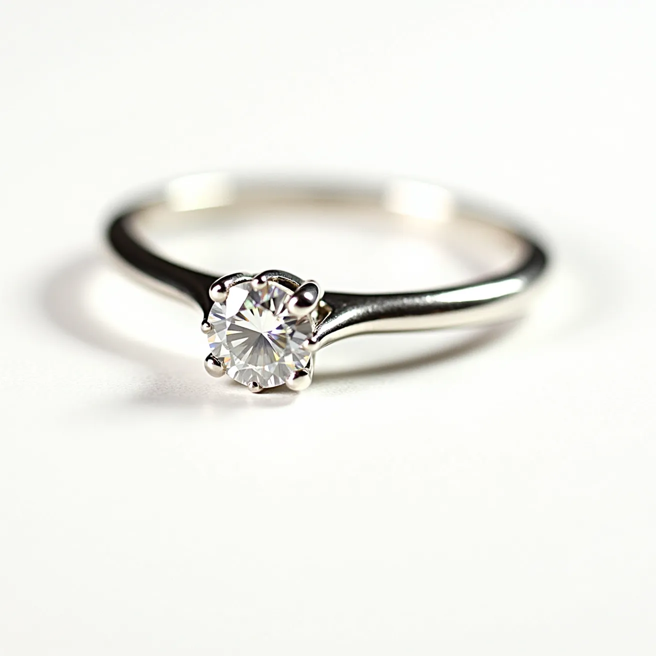 This engagement ring features a delicate and polished band, likely made of white gold or platinum, showcasing a classic and timeless design. The central gemstone is a round, brilliant-cut diamond, which is expertly mounted in a six-prong setting, allowing it to capture and reflect light from various angles. The prongs are sleek and slightly rounded, providing both security and elegance to the stone's presentation. Overall, the ring embodies a harmonious blend of simplicity and sophistication, making it a refined choice for an engagement ring.