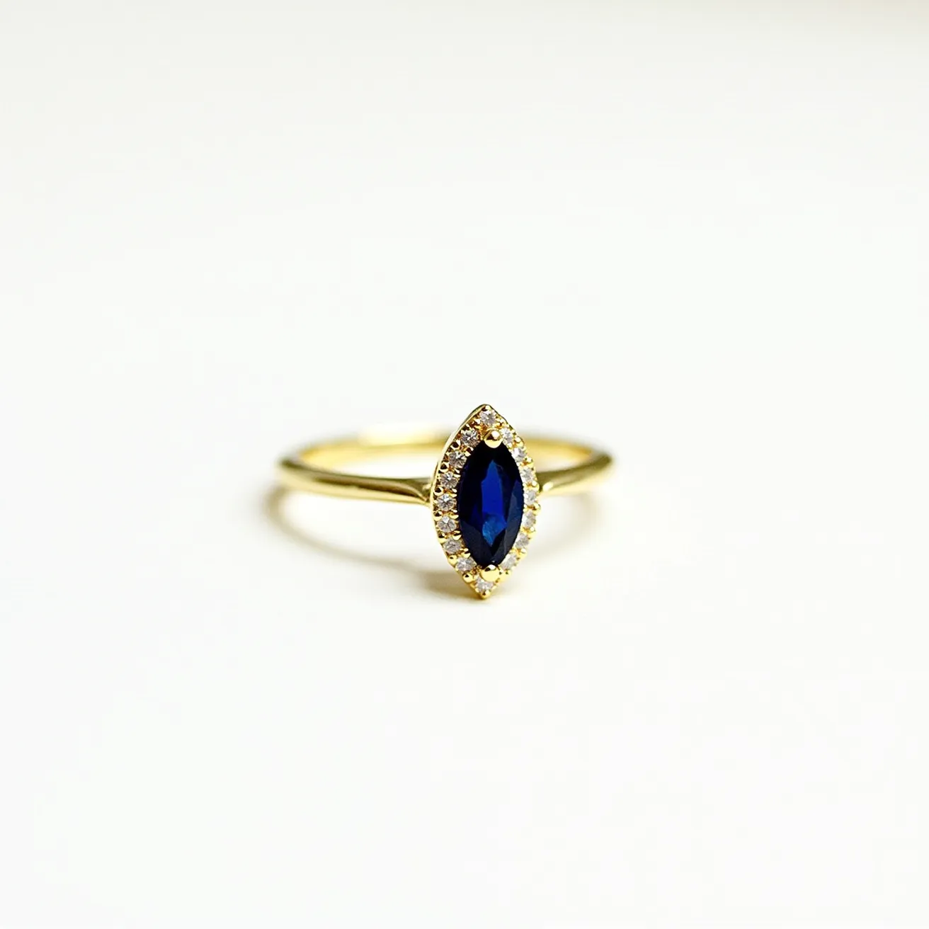 This engagement ring features a marquise-cut blue sapphire as its central gemstone, elegantly set in a halo setting of small round diamonds. The band appears to be made of yellow gold, enhancing the rich color of the sapphire and providing a classic, warm backdrop for the surrounding diamonds. The diamonds are meticulously arranged to encircle the sapphire, highlighting its shape and adding extra brilliance. The setting appears secure, with the diamonds set flush around the sapphire, creating a seamless and refined appearance.