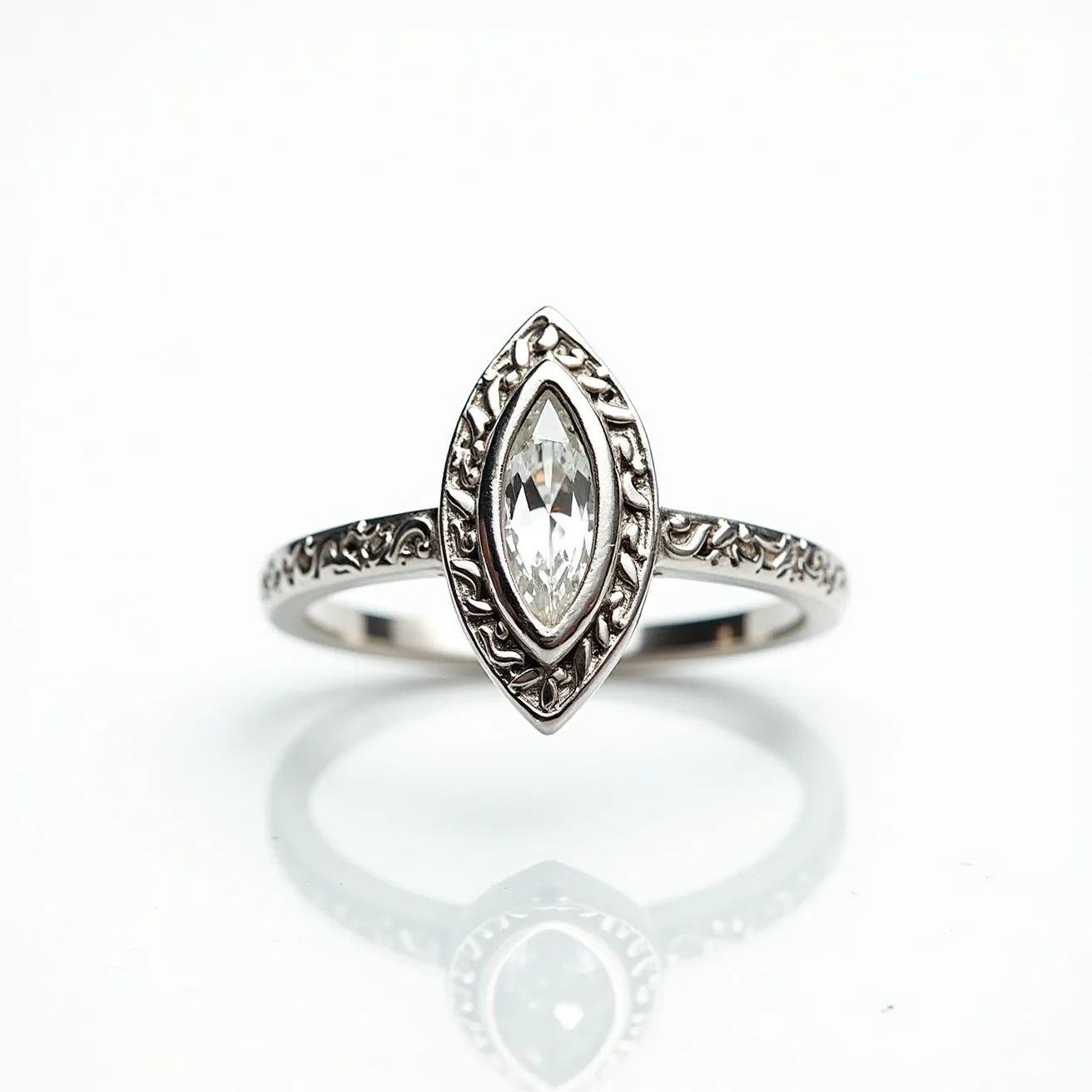 This engraved ring features a marquise-cut gemstone, likely a diamond, set centrally in a bezel setting. The band is crafted from a silvery metal, possibly white gold or platinum, and is adorned with intricate, floral engravings that enhance its elegance and vintage charm. The absence of a clasp or attachment signifies a classic, continuous band design, allowing the focus to remain on the central gemstone and detailed engravings.