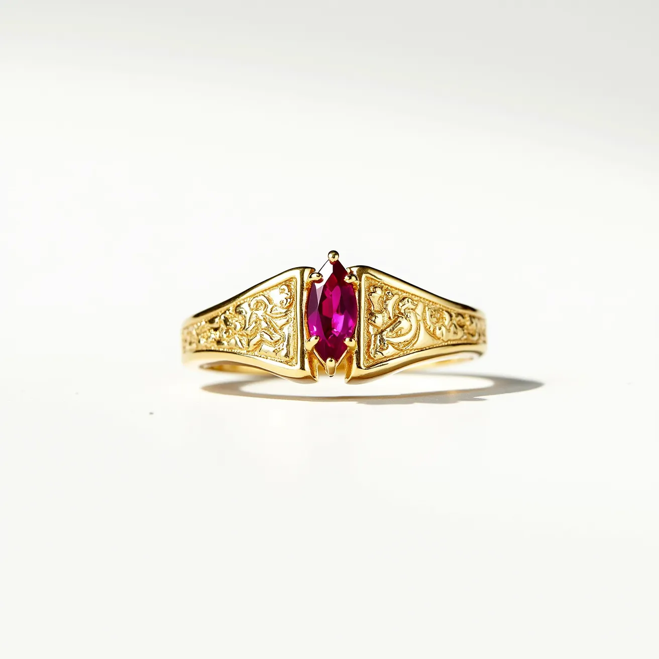 This engraved ring features an intricate design crafted from a gold material, exhibiting an ornate pattern along the band. At its center, the ring showcases a marquise-cut gemstone, likely a ruby or a similarly colored stone, set securely in a prominent prong setting. The combination of the vibrant stone and detailed gold work highlights its elegant and rich appearance. The band seamlessly connects in a continuous loop, characteristic of traditional ring designs.