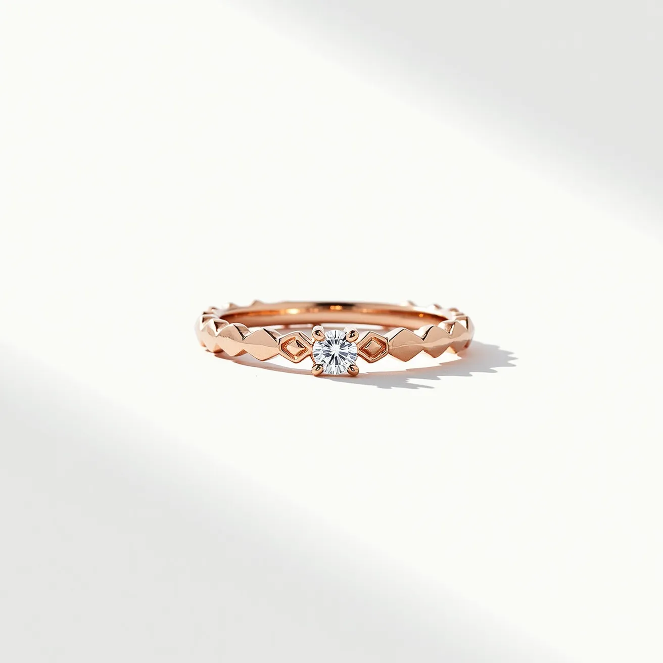 This eternity band ring is crafted from a warm rose gold material, featuring a unique pattern of faceted, diamond-shaped engravings along the band. Centrally set into the ring is a round-cut diamond, showcased in a secure prong setting that emphasizes its brilliance. The design does not incorporate any clasps or attachments, maintaining a continuous and seamless circular form symbolic of eternity.