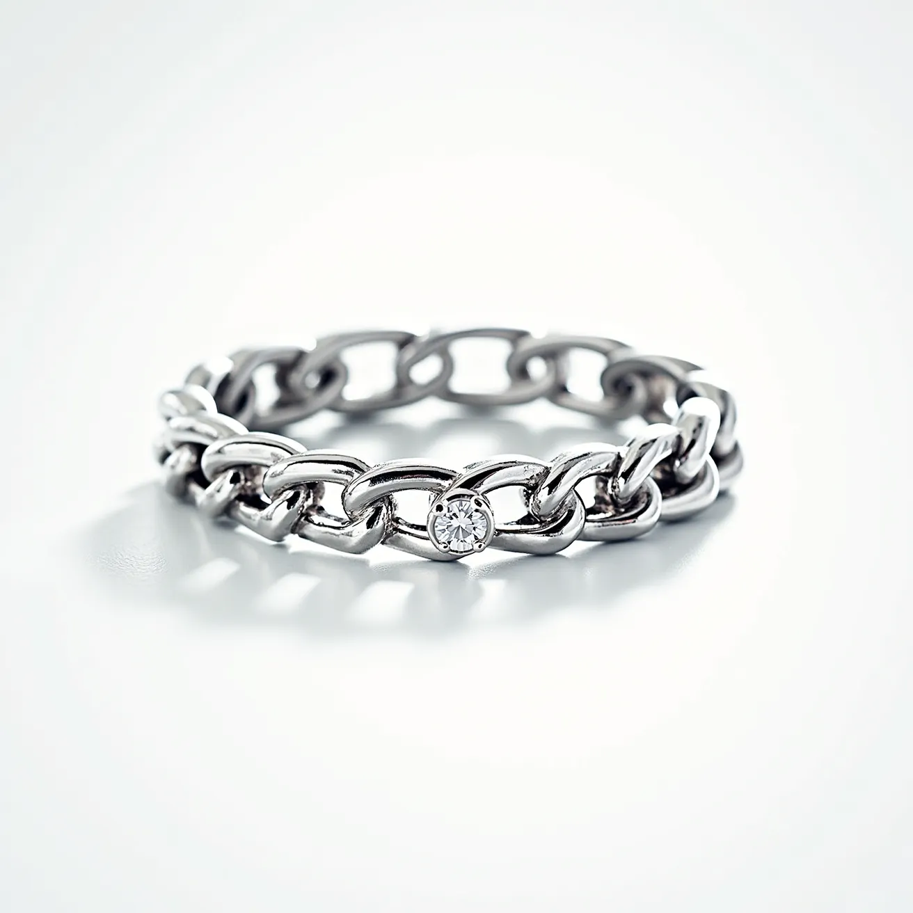 This eternity band ring features an intertwined chain-link design crafted from a lustrous metal, possibly white gold or silver, that creates a sleek and modern appearance. Nestled between the links is a round brilliant-cut diamond, set in a bezel that securely holds the gem, allowing its facets to disperse light brilliantly. The design's fluidity suggests a continuous motif with no visible clasps or breaks, embodying the concept of eternity in its seamless circular form. The combination of the metallic sheen with the sparkling diamond creates a striking contrast, enhancing both the elegance and contemporary style of the piece.