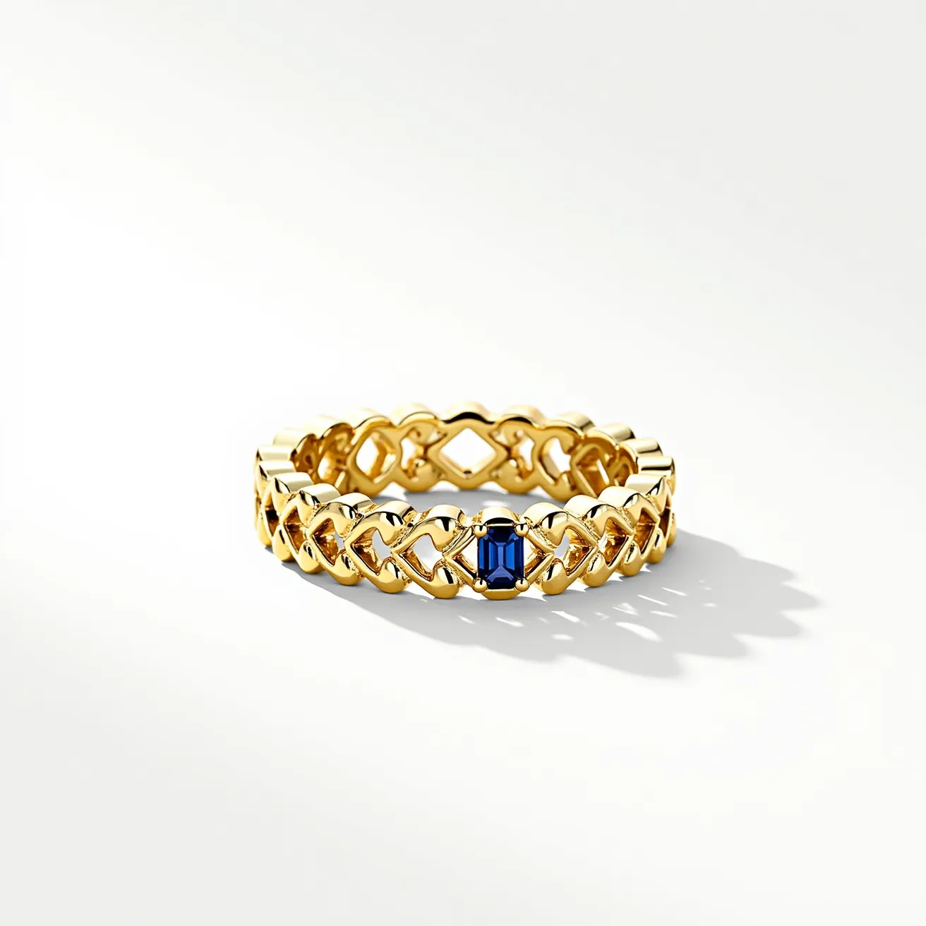 This eternity band ring features a gold band with an intricate, interwoven design that creates a continuous pattern around the entire ring. It has a striking blue gemstone, likely a sapphire, securely held in place with a rectangular cut and a prong setting. The setting enhances the gemstone's visibility and allows light to pass through, emphasizing its color and brilliance. There is no clasp, as the continuous pattern signifies the unbroken nature characteristic of eternity rings.