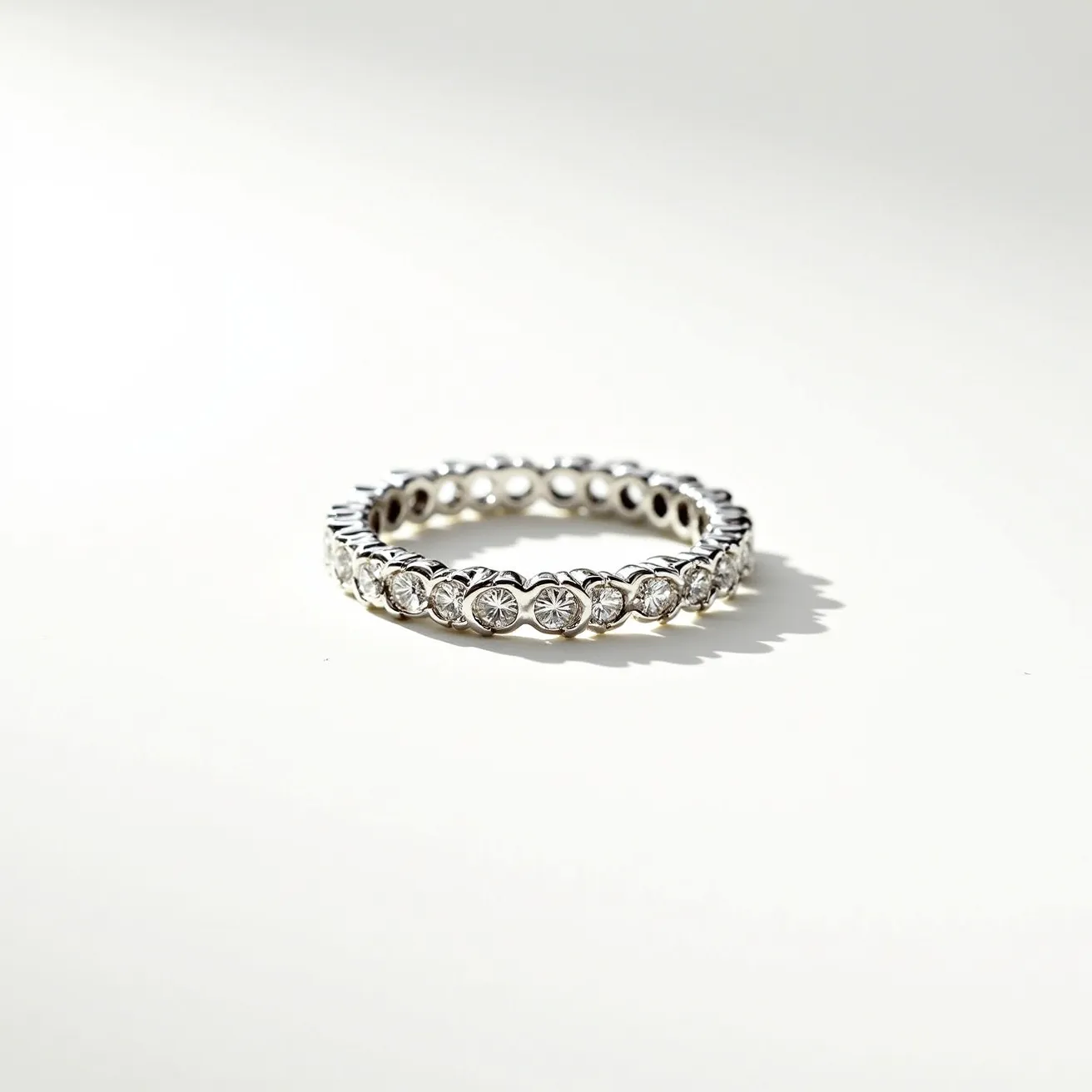 This eternity band ring features a seamless circle of round, brilliant-cut diamonds set in a continuous bezel setting. The gems are uniformly spaced around the entire band, giving it a harmonious and elegant appearance. The band itself is likely made of a lustrous metal, possibly platinum or white gold, complementing the clarity and sparkle of the diamonds. The bezel setting securely holds each stone in place while enhancing their brilliance and providing a modern aesthetic. The ring does not include a clasp or attachment, as is typical for eternity bands, emphasizing its uninterrupted, infinite design.