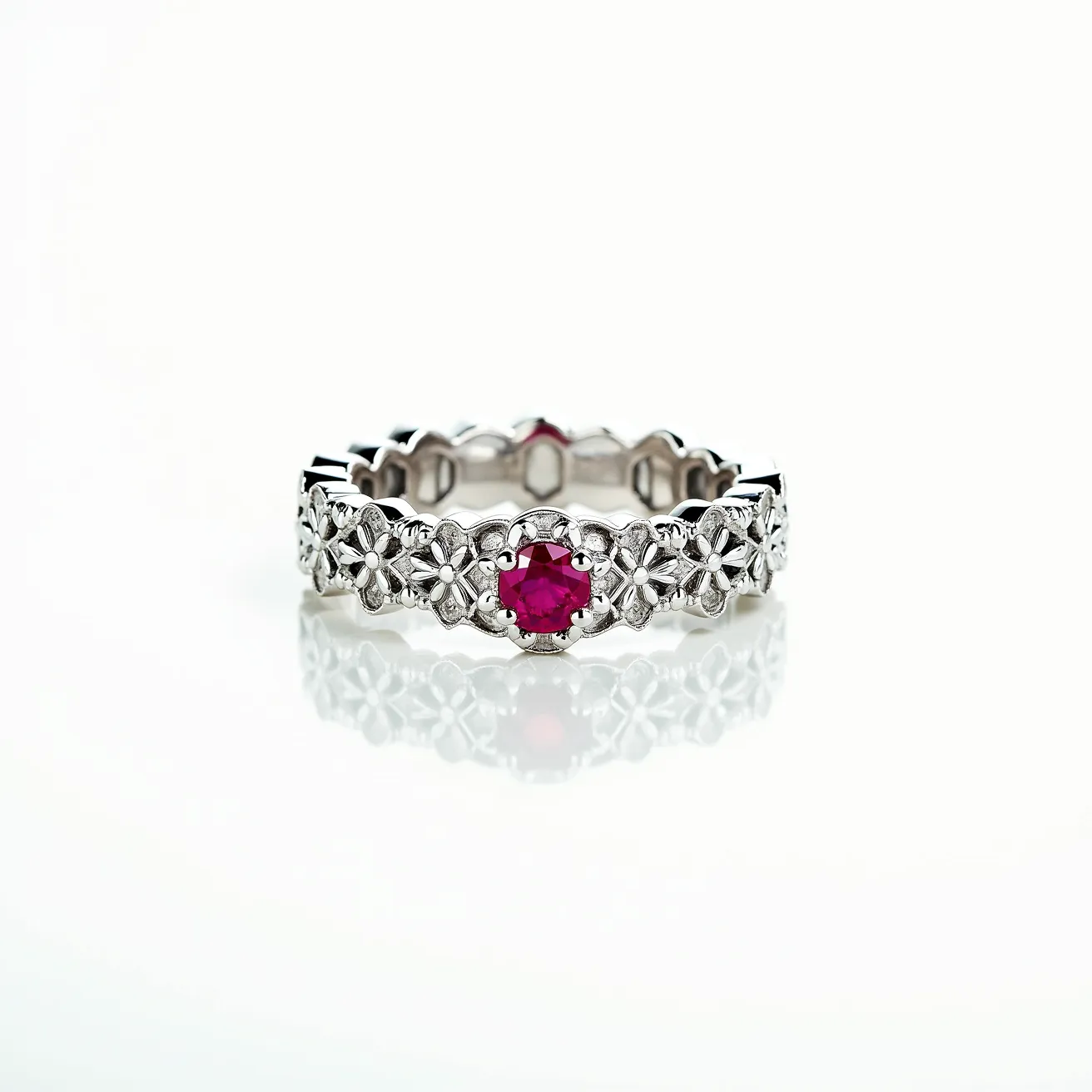 This eternity band ring features a delicate metal band, likely crafted from white gold or platinum, with a continuous pattern of intricate floral designs. Each flower is adorned with a small, central setting, enhancing the overall ornamental appeal. At intervals within the pattern, round-cut rubies are prominently set, adding vibrant bursts of red to the design. The gems are securely set within the floral motifs, ensuring they are showcased prominently in the band’s intricate structure. The ring has no visible clasp or attachment, typical of eternity bands, underscoring its seamless and eternal design.