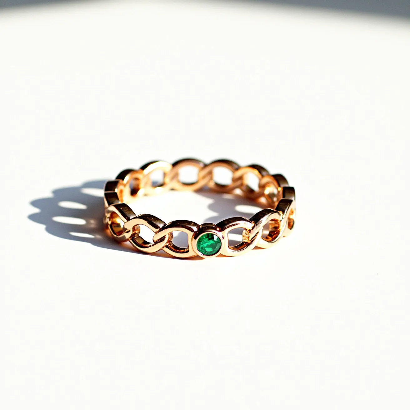 This eternity ring features a series of interlocking gold links that form a continuous band. Each link securely holds a single round emerald, cut to showcase its rich green hue. The emeralds are set in a simple yet elegant bezel setting, allowing them to be the focal point without the need for additional embellishment. The design is seamless, with no visible clasp or attachment, emphasizing the ring's symbolism of eternal connection and continuity.