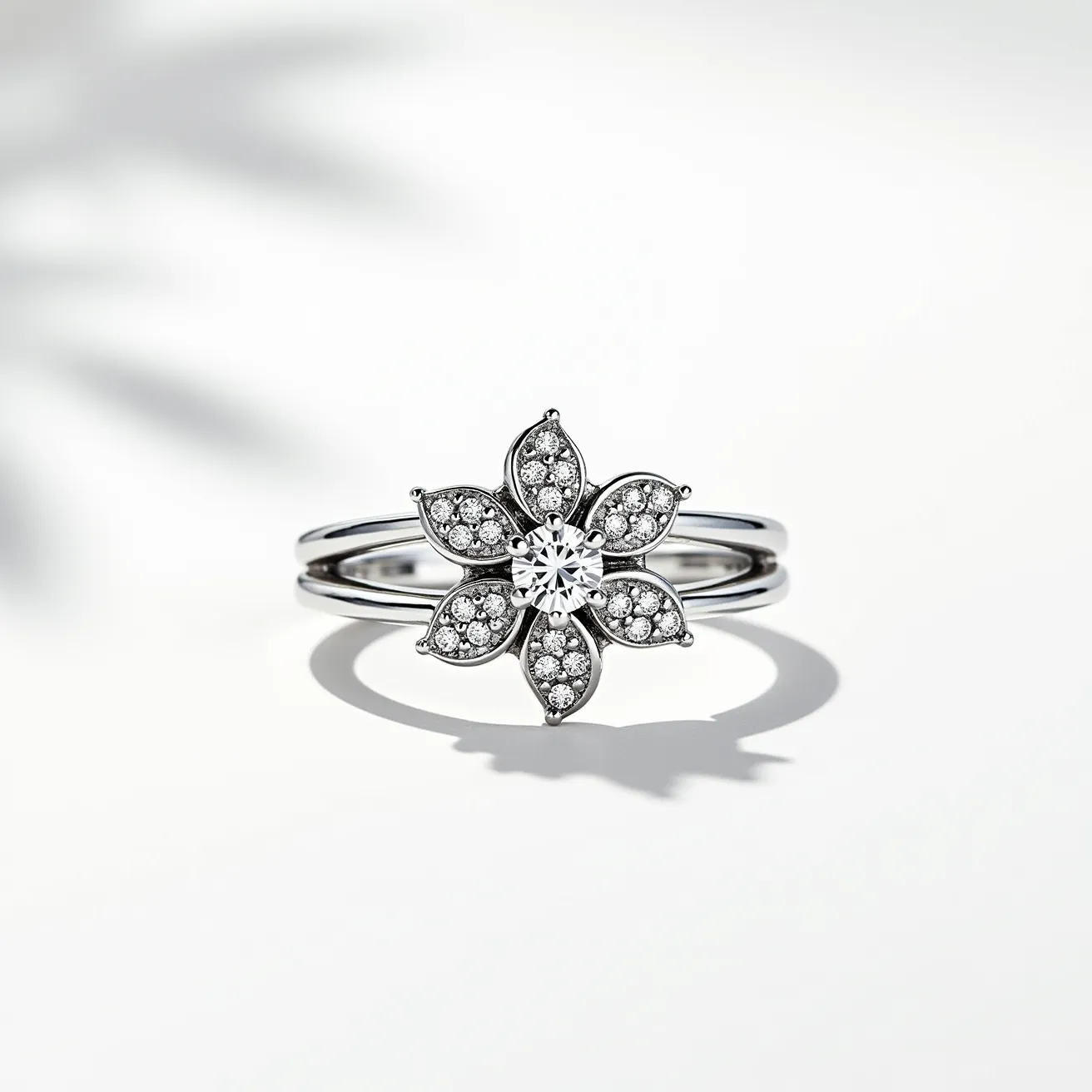 This floral ring features a delicate flower design, crafted from what appears to be a high-quality metal, possibly white gold or platinum, giving it a sleek and elegant appearance. At the center of the floral motif is a round-cut diamond, held securely in a prong setting, which serves as the focal point of the piece. Surrounding the center stone are intricately designed petals, each encrusted with smaller round diamonds, accentuating the ring's sparkle and adding depth to the floral design. The ring band splits into two slender strands, enhancing its delicate aesthetic while providing additional structural integrity. The overall craftsmanship highlights both the central diamond and the surrounding intricate details, creating a harmonious and eye-catching design.