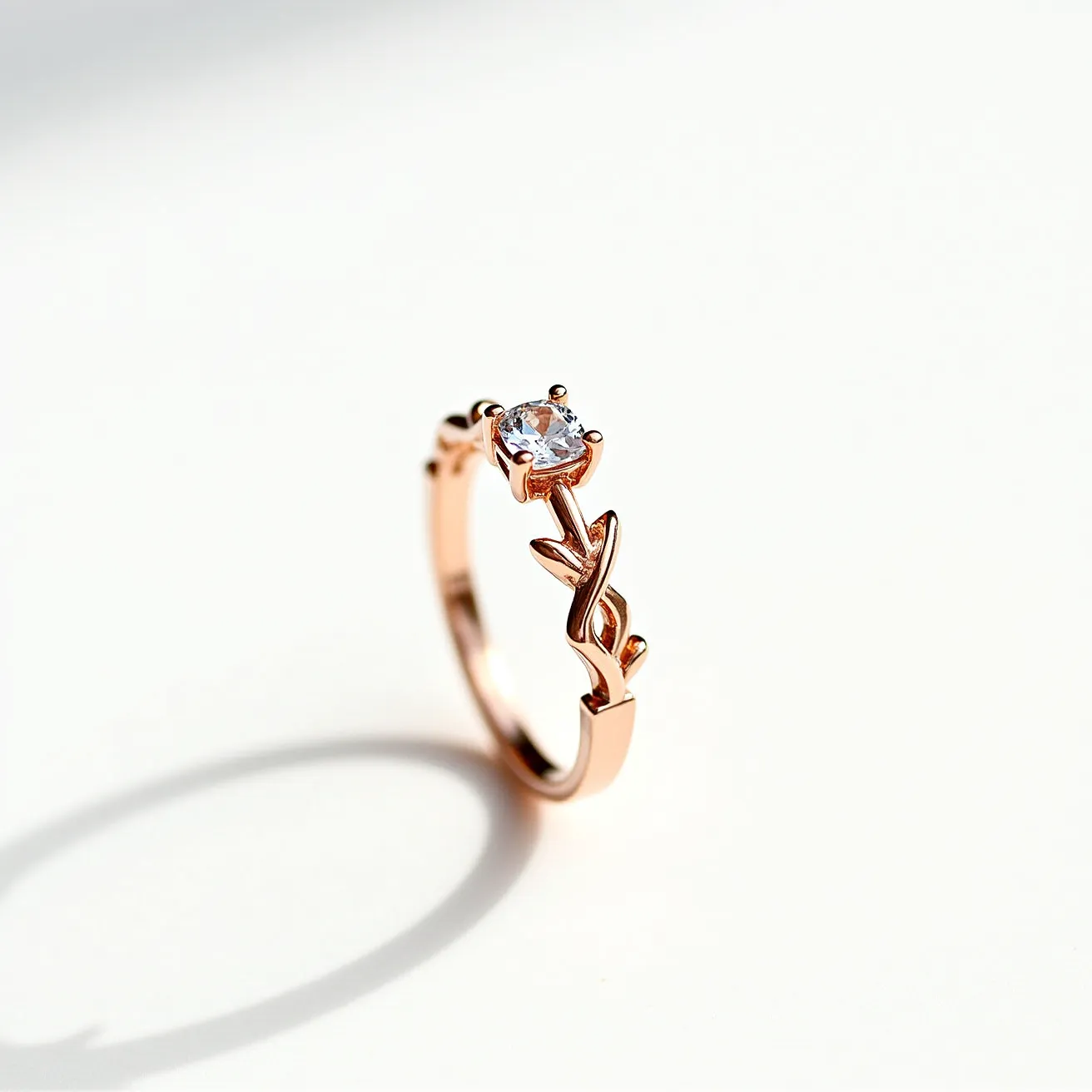 This floral ring features an elegant, rose gold band that gracefully incorporates a leaf-like design along its structure, emphasizing a nature-inspired aesthetic. At the center, a round-cut transparent gemstone is securely set in a classic four-prong setting, acting as the focal point of the piece. The prongs are crafted from the same rose gold material as the band, providing a cohesive and harmonious design. The ring does not feature a clasp, as it is a complete band meant to be slipped onto the finger. The combination of the rose gold and the clear gemstone creates a timeless and delicate piece of jewelry.