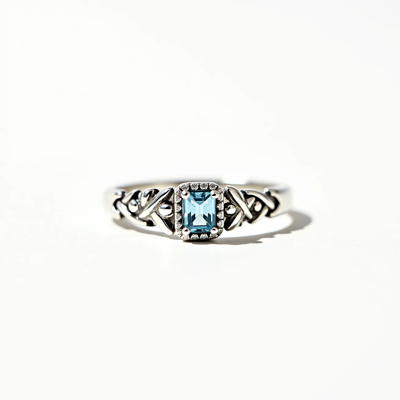 This friendship ring is crafted from a silver metal, featuring a central gemstone with a light blue hue, likely an emerald-cut aquamarine. The gemstone is set in a decorative prong setting that enhances its sparkle and security. The band is adorned with intricate Celtic knot designs, adding an elegant and meaningful touch to the piece, symbolizing unity and friendship. There are no visible clasps or attachments, consistent with traditional ring design.