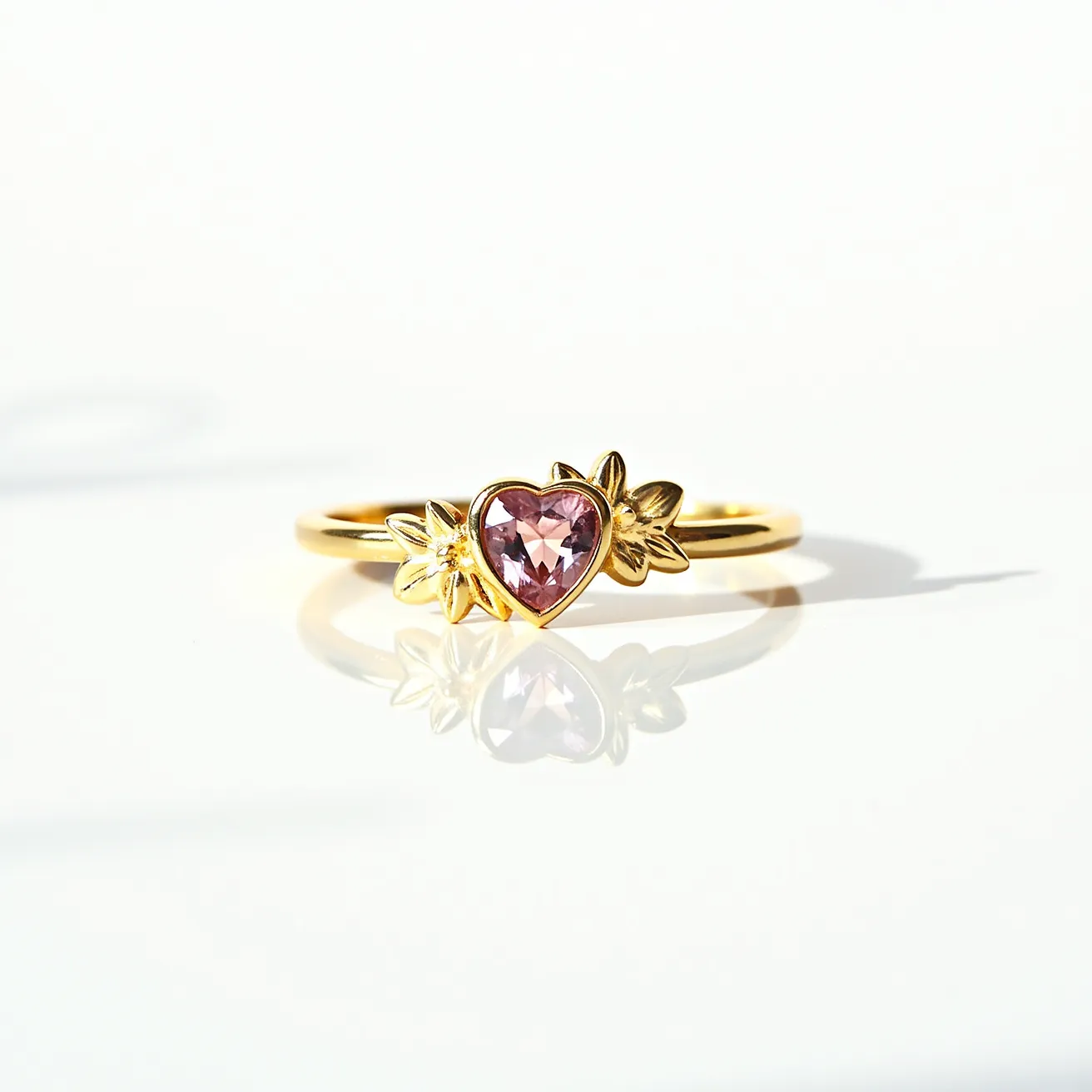 This friendship ring features a delicate gold band adorned with a heart-shaped pink gemstone as its centerpiece. The stone is secured in a bezel setting, providing a smooth and elegant look. Flanking the gemstone are two intricately designed flower motifs, adding a natural and whimsical touch to the overall design. The use of gold for the band and setting complements the soft hue of the pink stone, enhancing its brilliance and creating an elegant aesthetic.