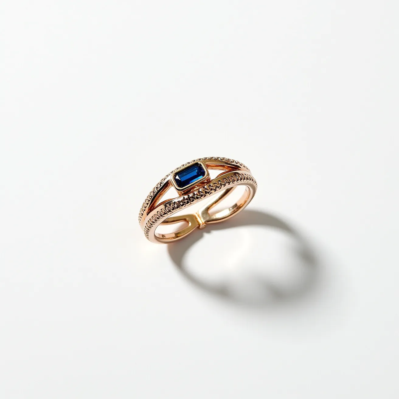 This friendship ring features a rich gold band intricately designed with a braided pattern, exuding a sense of elegance and detail. The centerpiece is a deep blue rectangular-cut gemstone, likely a sapphire, held securely in a bezel setting that emphasizes its color and clarity. The ring is crafted with meticulous attention to texture and symmetry, providing both visual appeal and symbolic significance. The dual band design adds a layer of sophistication, making it a striking piece that captures the essence of cherished bonds.