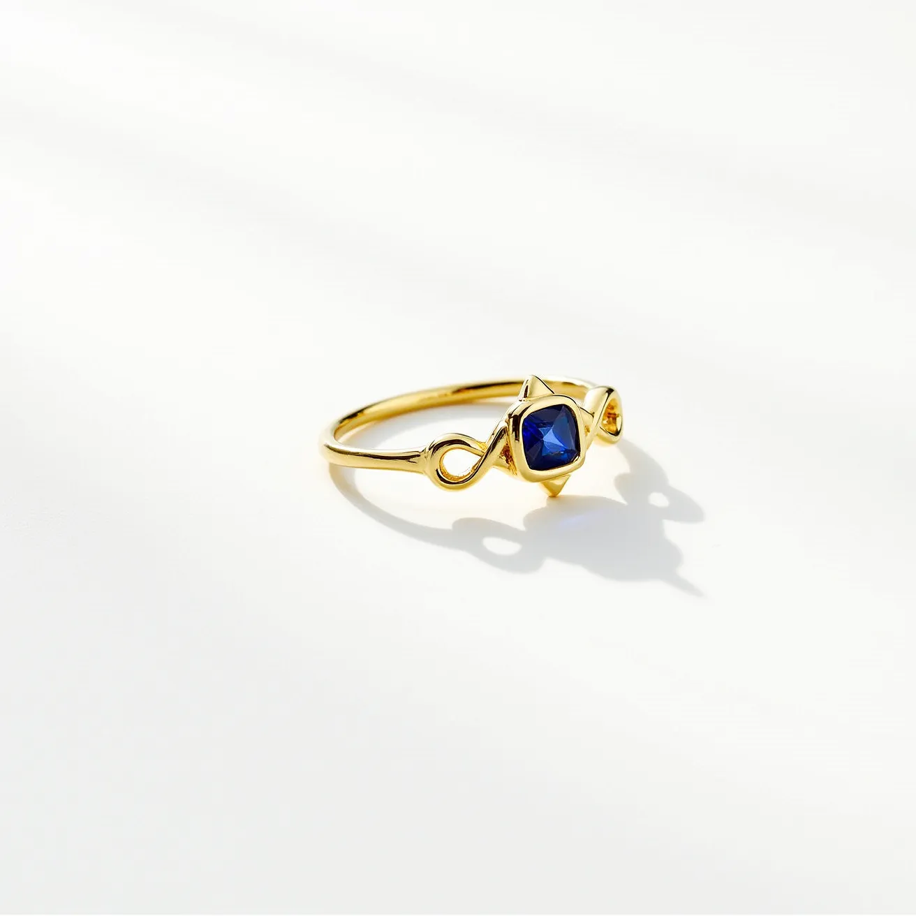 This friendship ring features a delicate band crafted from yellow gold, characterized by its smooth and polished finish. At its center, the ring showcases a beautiful blue sapphire, cut into a square shape. The sapphire is set in a bezel-style setting, securely encasing the stone while allowing its facets to catch the light. The ring incorporates an infinity loop design on each side of the gemstone, adding a symbolic and elegant touch to its overall appearance.