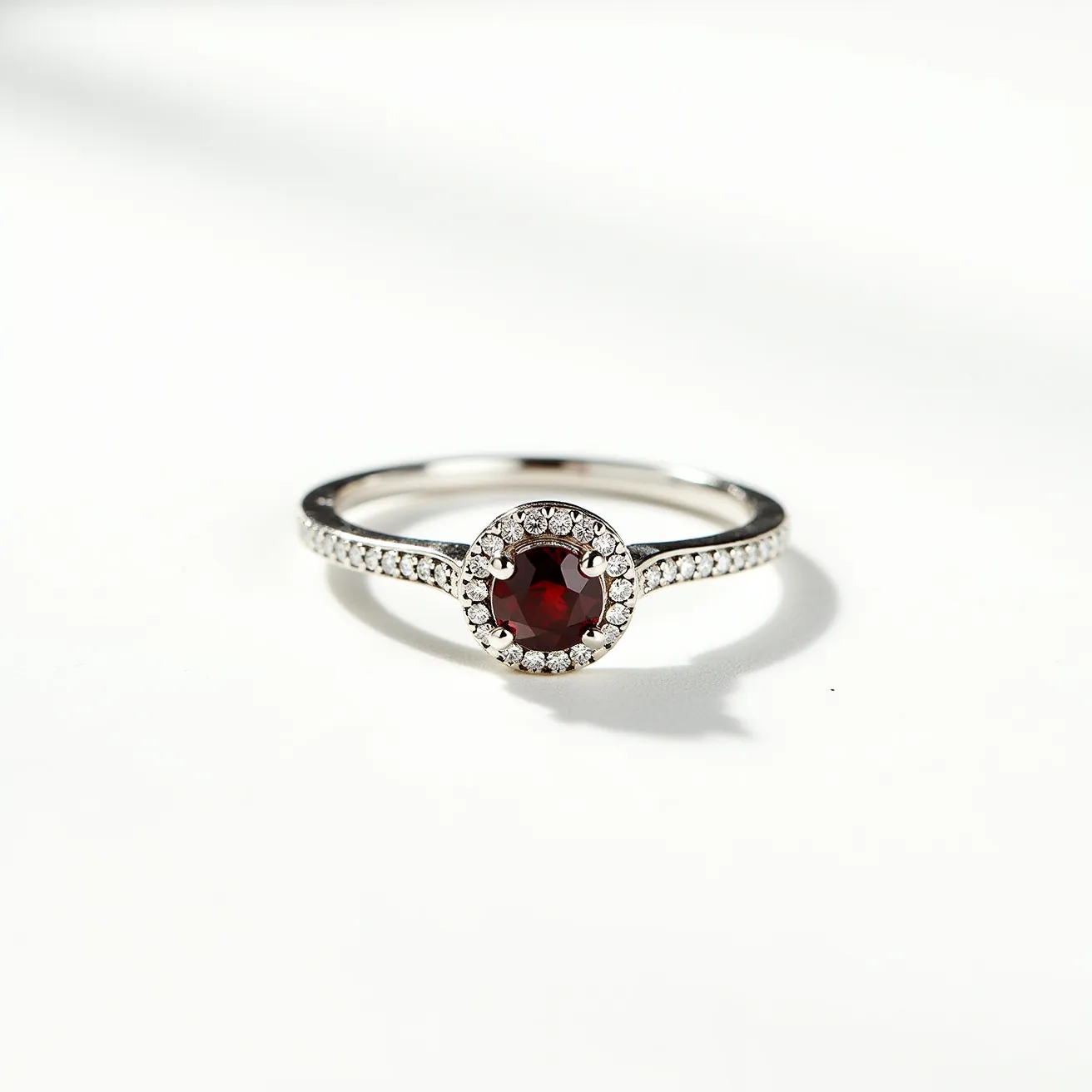 This garnet engagement ring features a striking round-cut garnet as its center stone, radiating a deep, rich red hue. The garnet is elegantly set in a halo setting, surrounded by smaller clear gemstones that enhance its brilliance and create a captivating contrast. The band of the ring is crafted from a polished metal, possibly white gold or platinum, lending it a sleek and modern look. Adorning the band are additional small, clear stones, adding a touch of sparkle along the sides. The overall design of the ring combines classic elegance with contemporary elegance, making it a beautiful and sophisticated choice for an engagement ring.