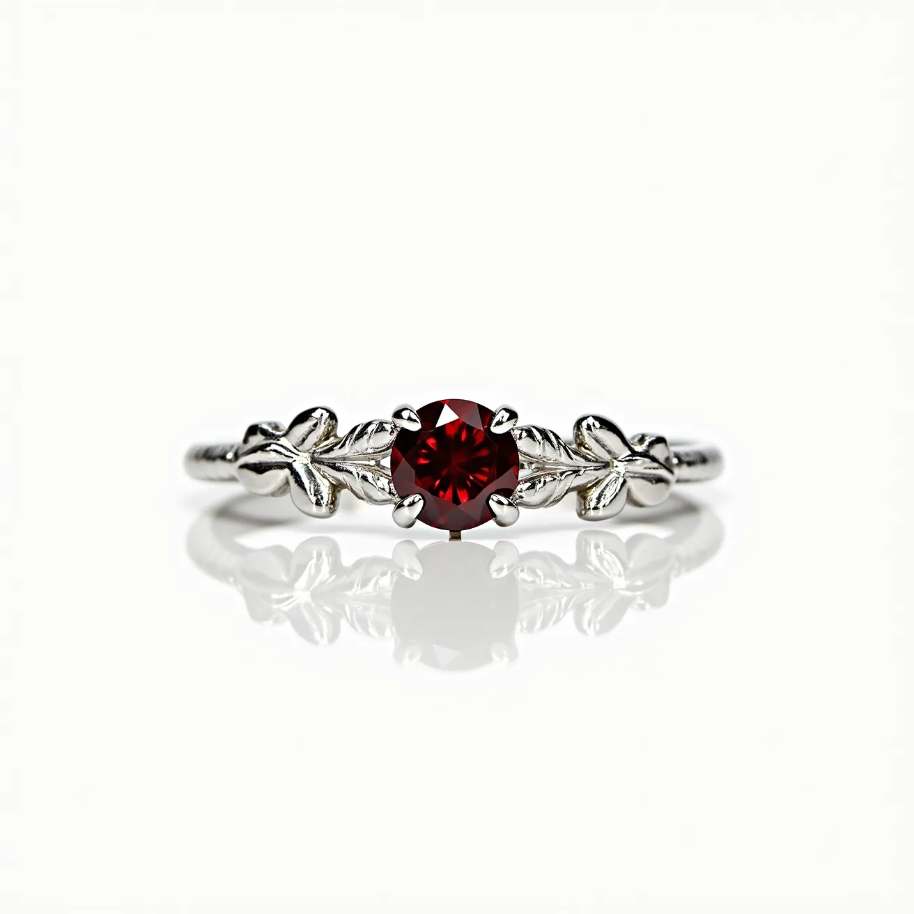 This garnet engagement ring features a central round-cut garnet gemstone, set in a delicate prong setting that highlights its deep red hues. The band is crafted from a lustrous silver-colored metal, designed with intricate leaf motifs on either side of the stone, adding an elegant, nature-inspired touch to the overall design. The detailing on the band complements the garnet, emphasizing a harmonious blend between the gemstone and the intricate metalwork.